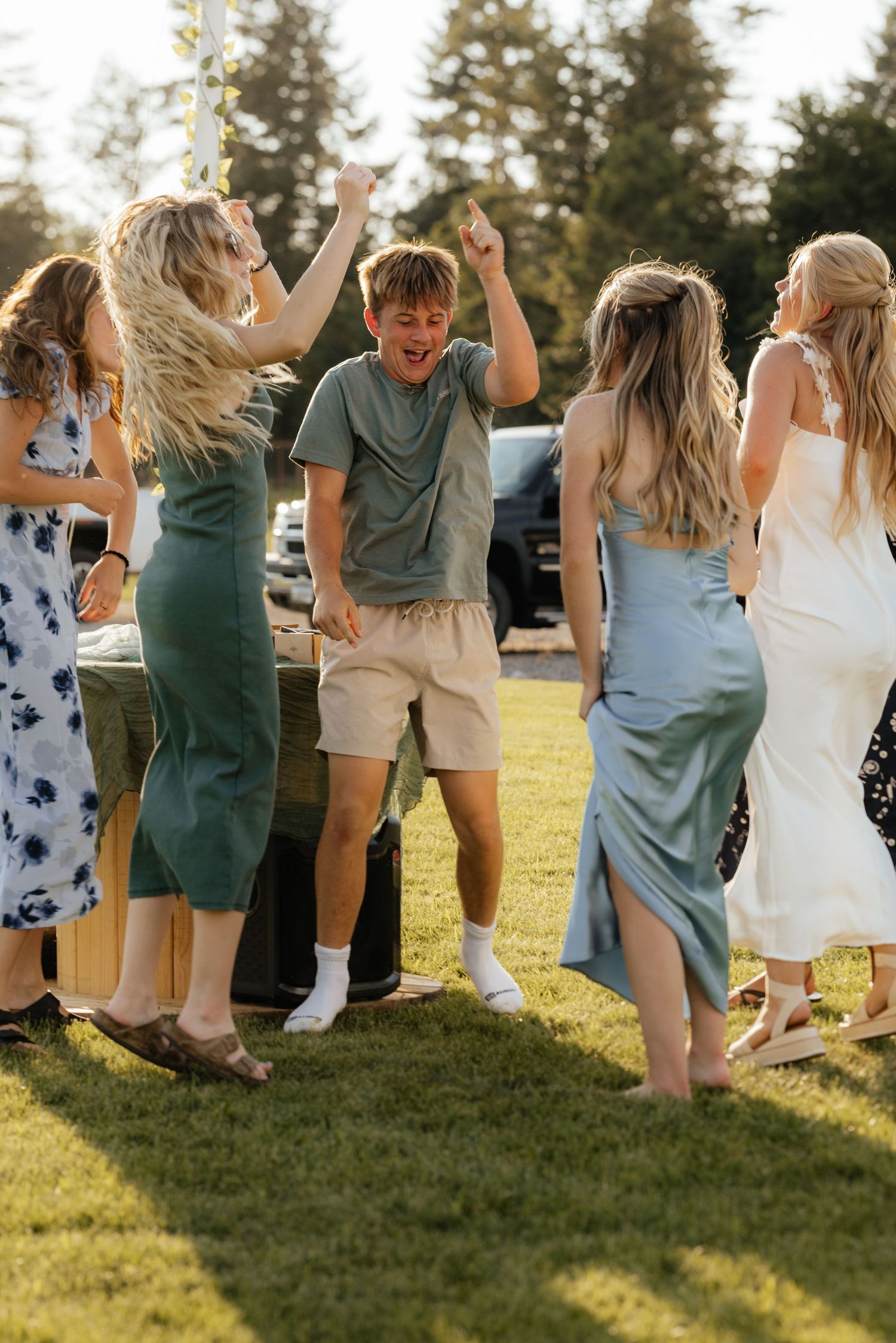A group celebrates joyfully on a grassy lawn during sunset with long shadows cast across the ground.