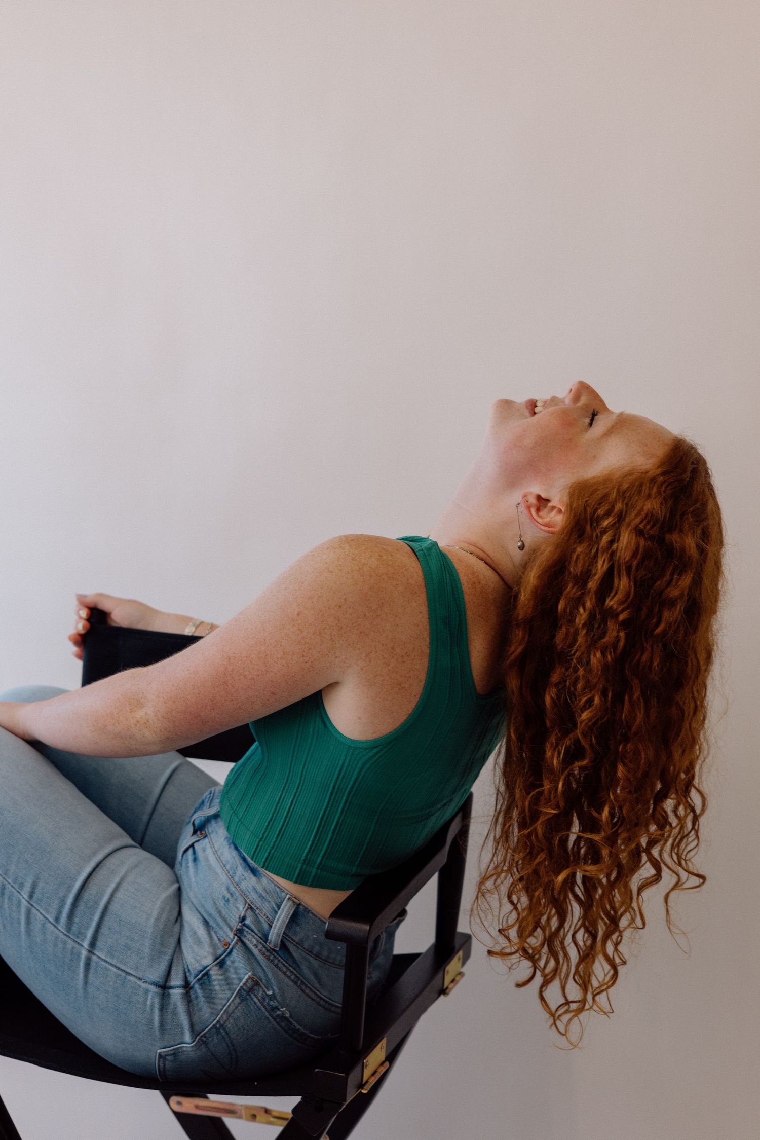 A curly-haired person in a green top leans back dramatically in an artistic portrait series.