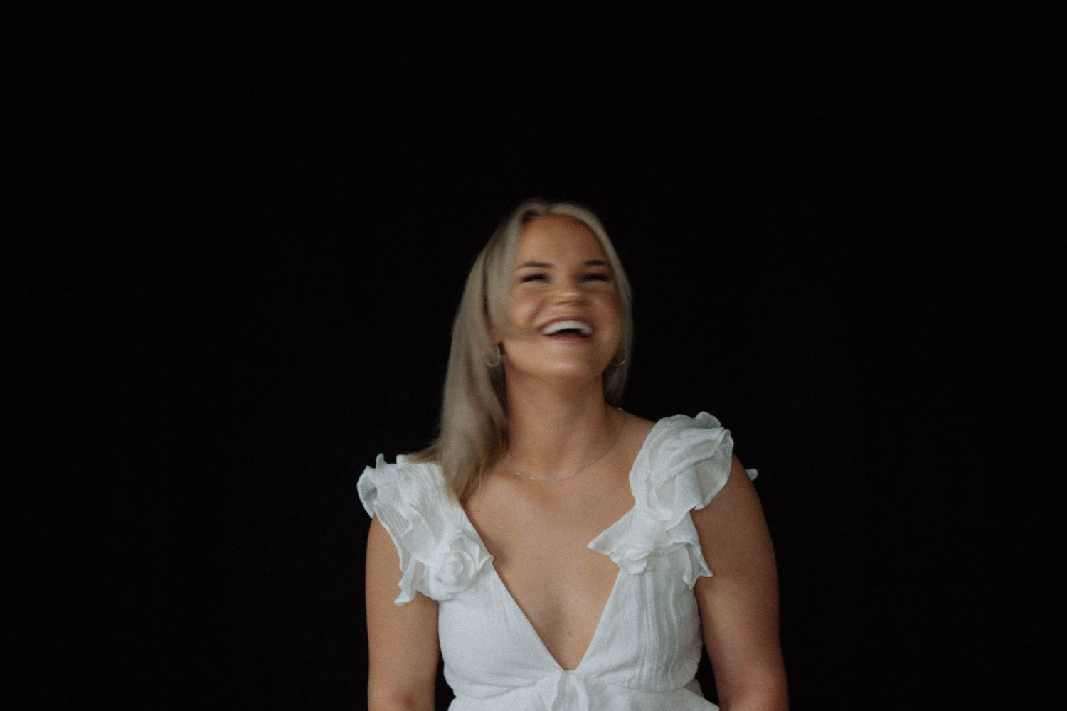 A person in a white ruffled dress smiles while posing against a dark background.