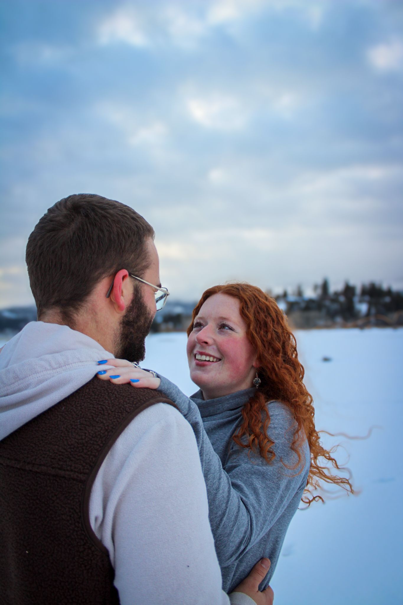 A couple in winter clothing share an intimate moment together against a snowy landscape.