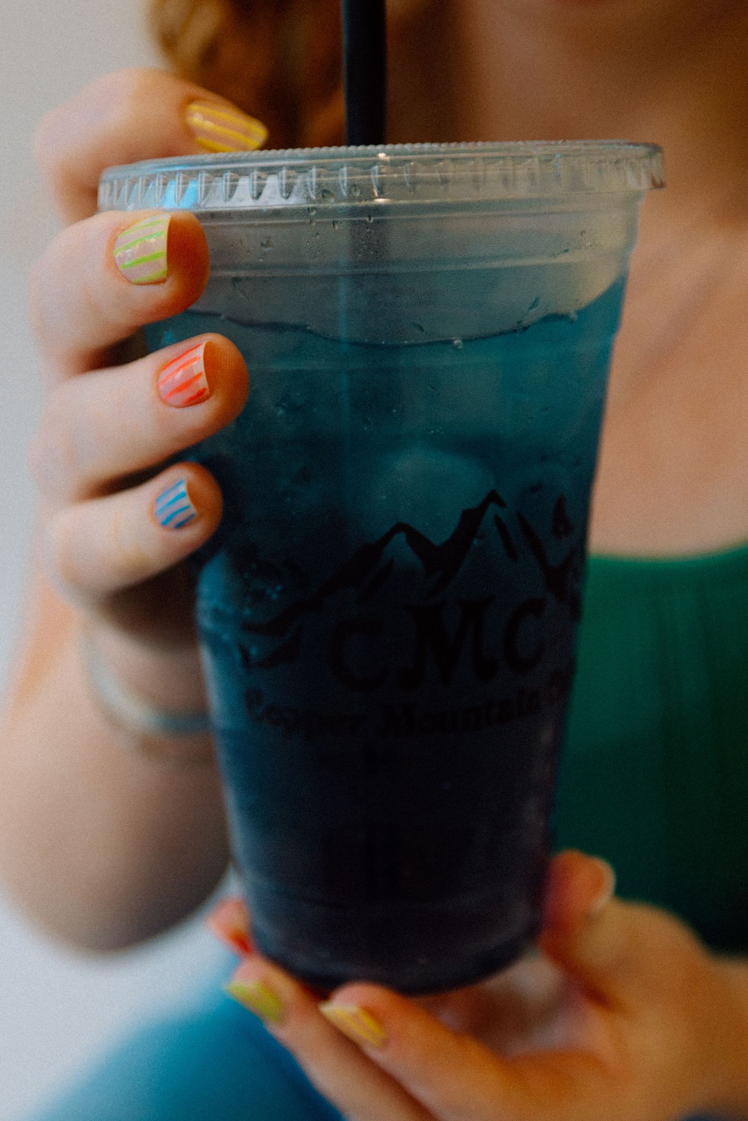 Close-up of hands holding blue iced drink with colorful nail polish.
