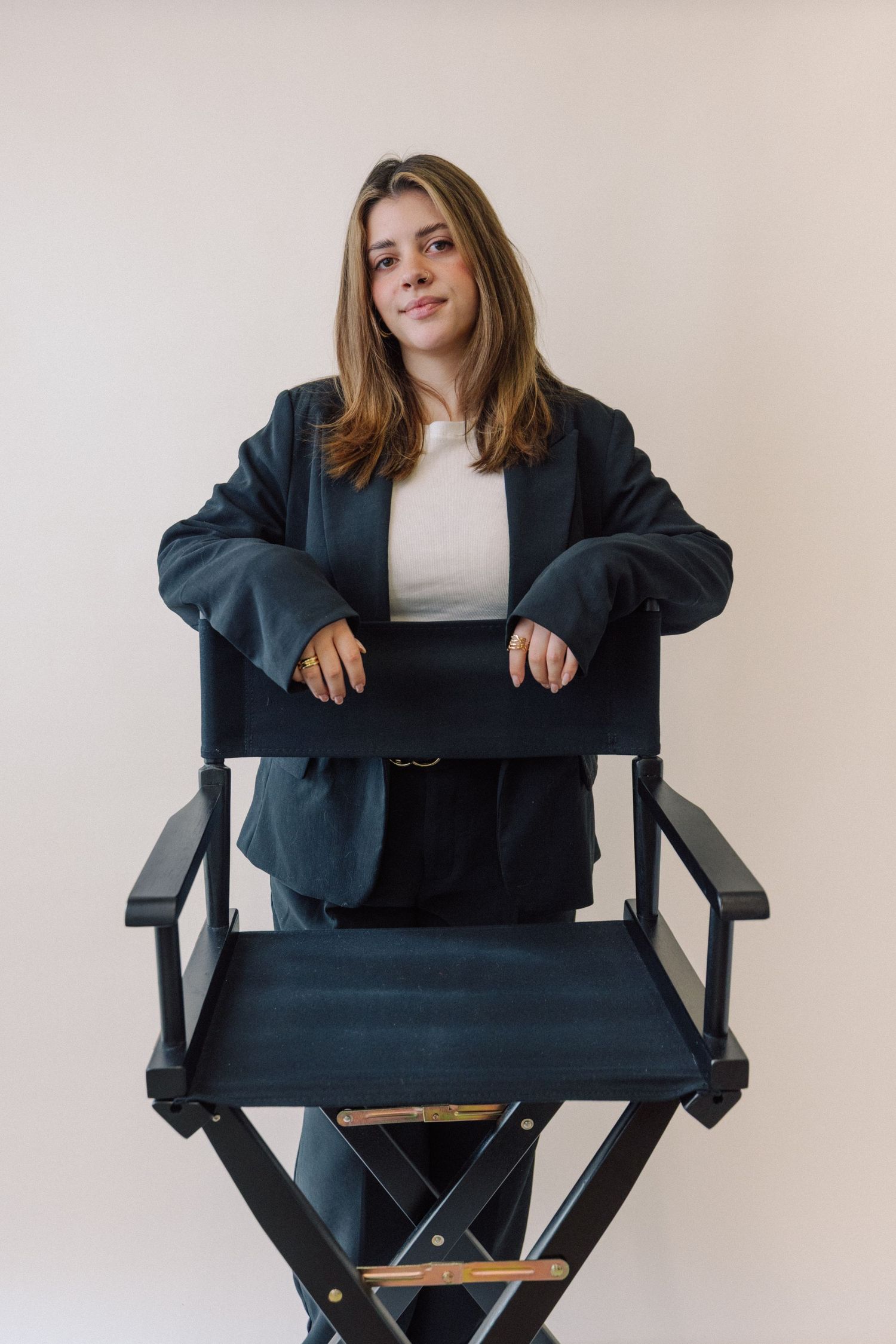 Professional seated in a director's chair wearing a navy blazer and white top against a light background.
