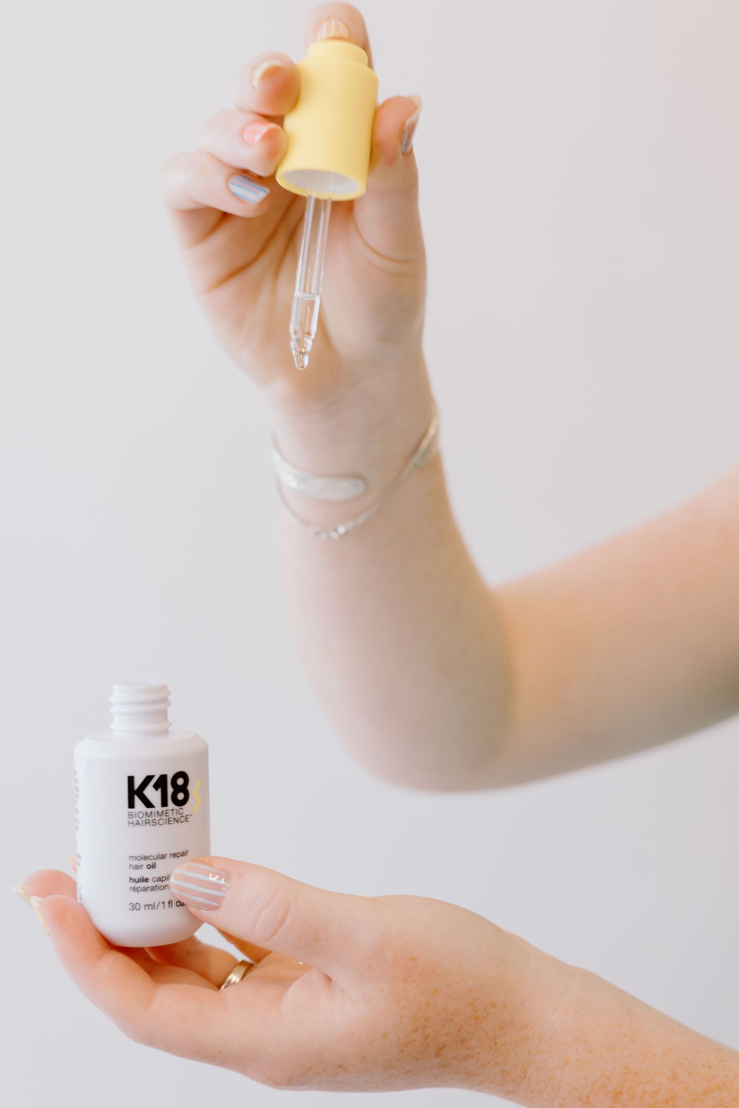Hands demonstrating use of white skincare product K18.