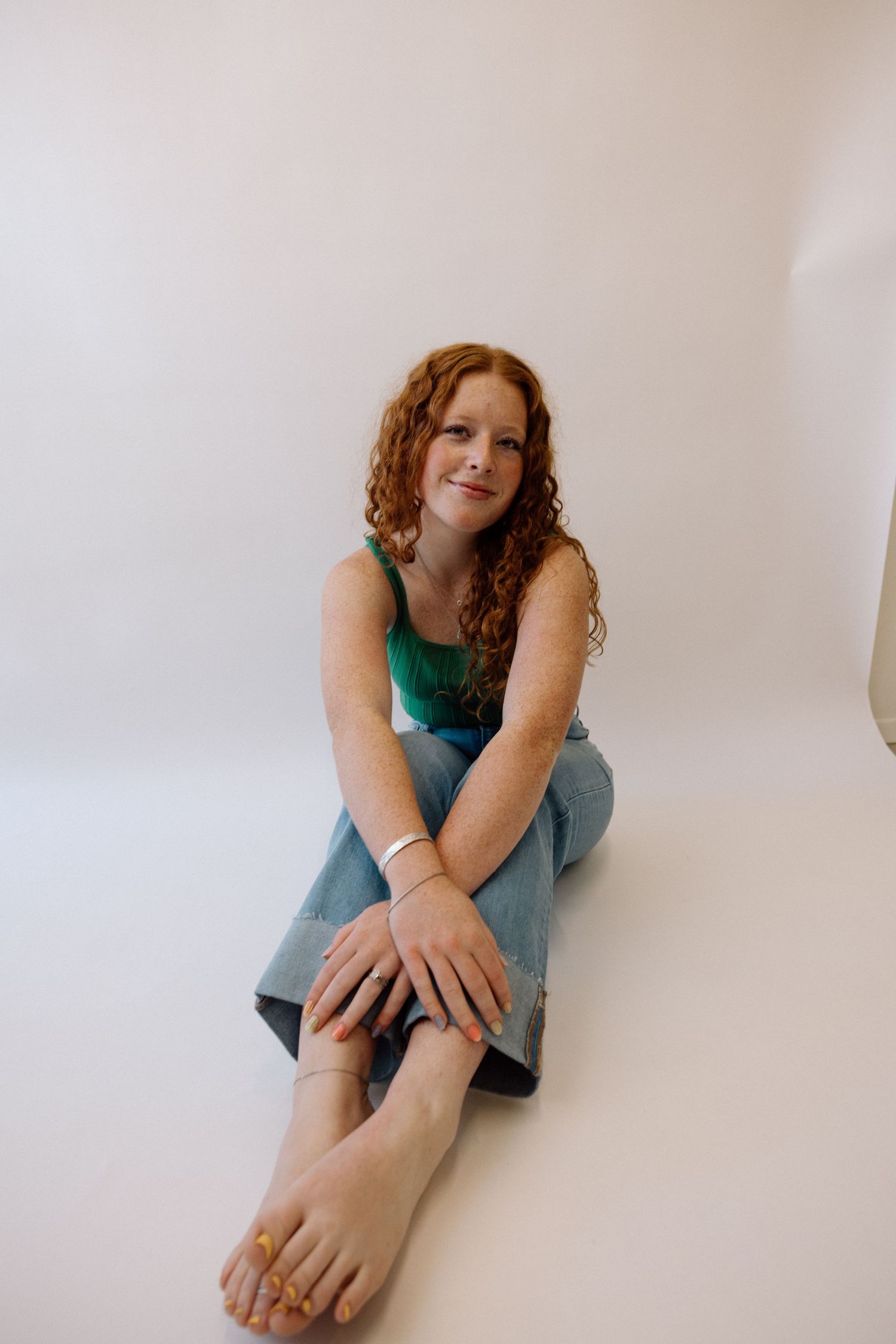 Person in teal top and jeans sits casually against white background.