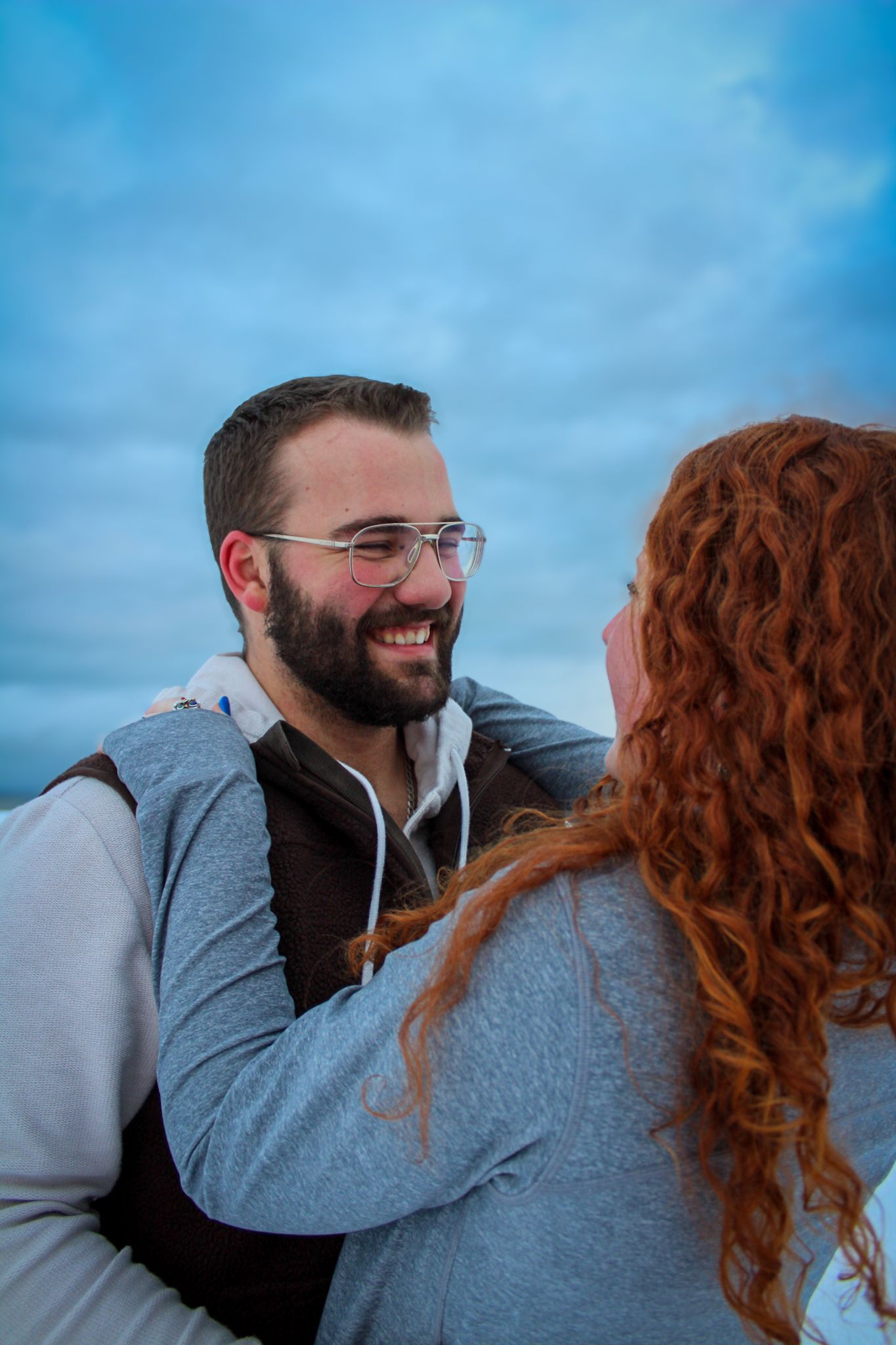 Couple embraces lovingly against winter sky backdrop during romantic photoshoot.
