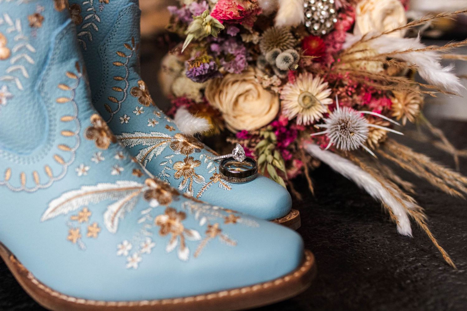Vintage blue leather boot decorated with dried flowers and gold embellishments against a dark background.
