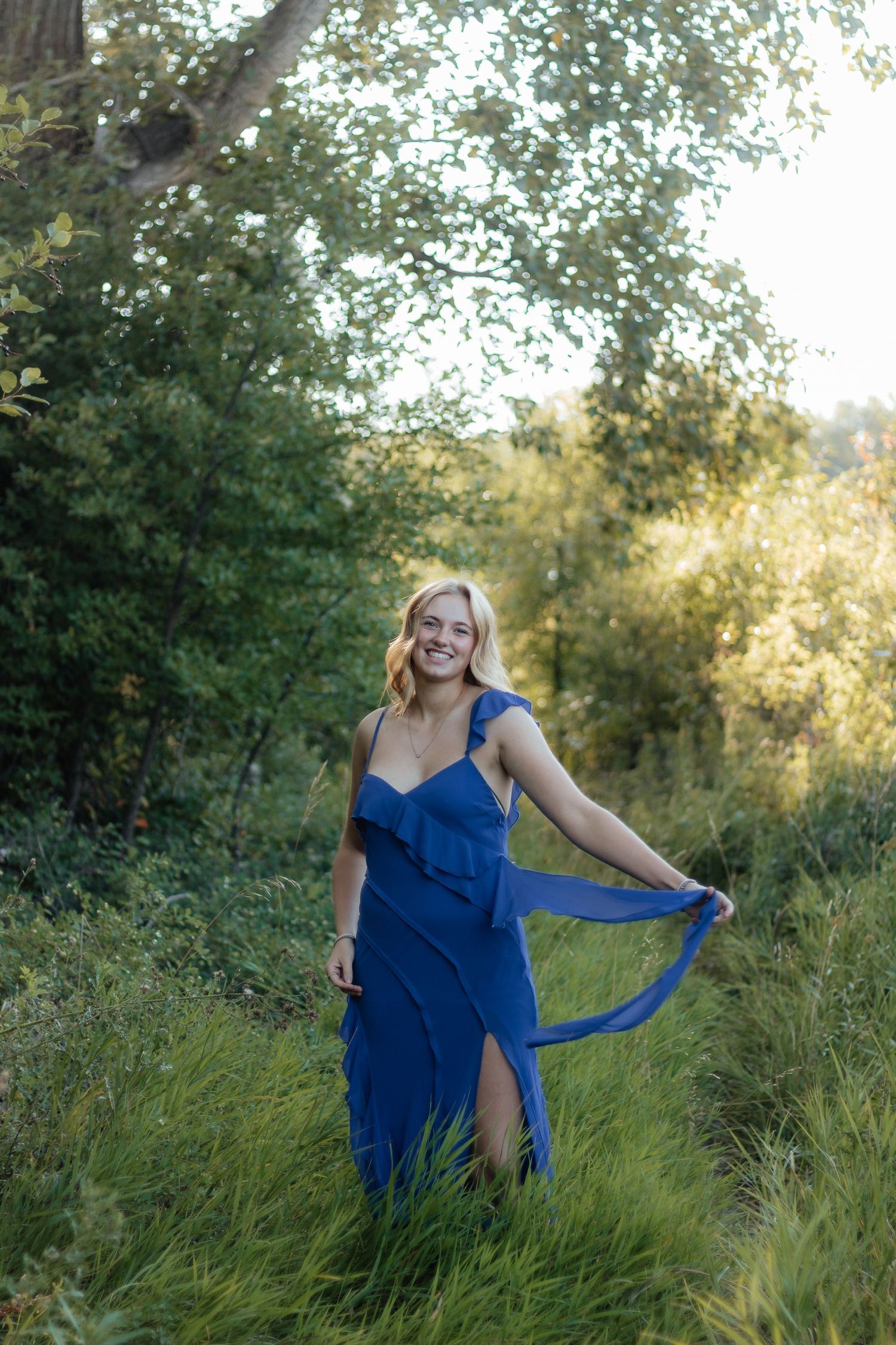 A flowing blue dress moves gracefully in a natural outdoor setting with sunlit greenery.