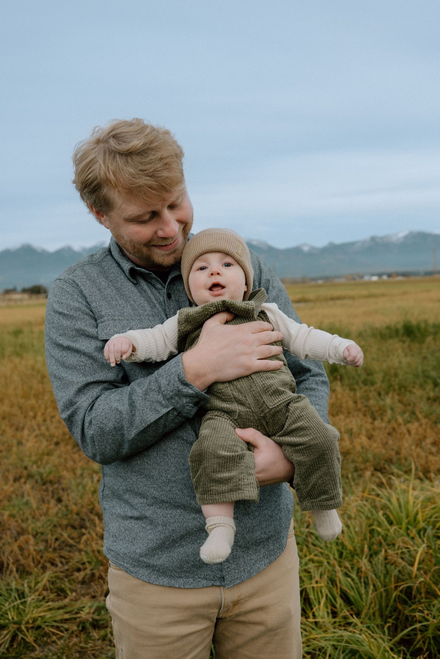 A heartwarming moment in a grassy field with mountains in the background on an overcast day.