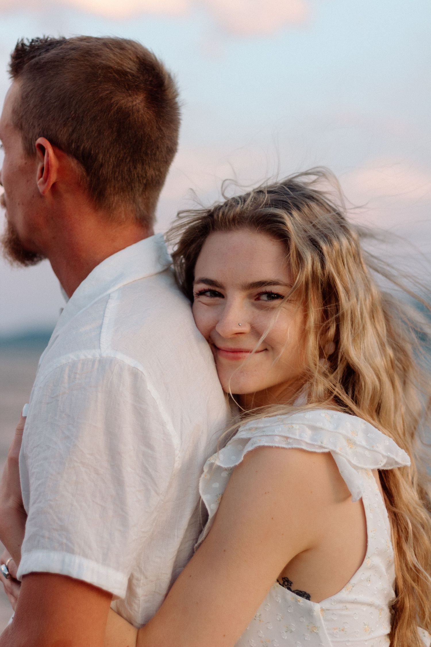 Couple in white clothing sharing tender moments during sunset photoshoot.
