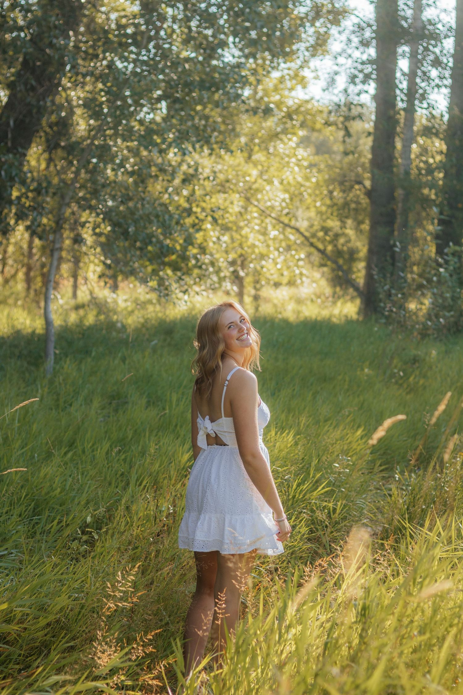 A dreamy summer scene shows someone in a white dress walking through tall golden grass in a sun-dappled forest.