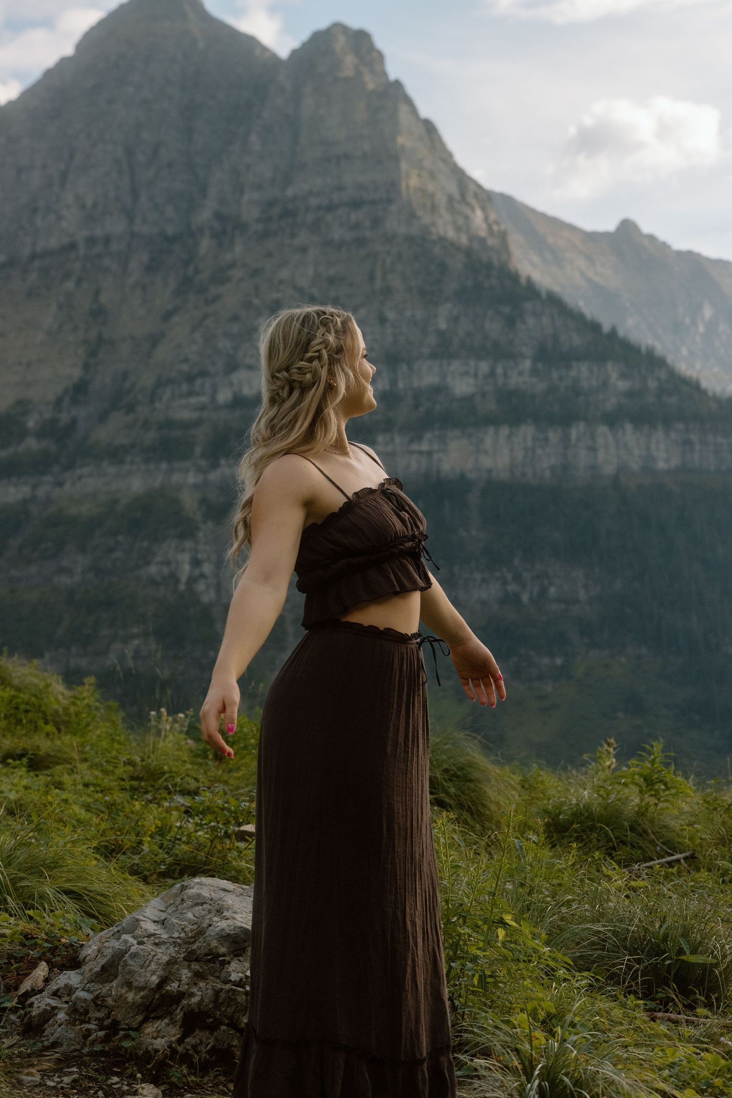 A black dress flows gracefully against rugged mountain cliffs in a natural outdoor setting.