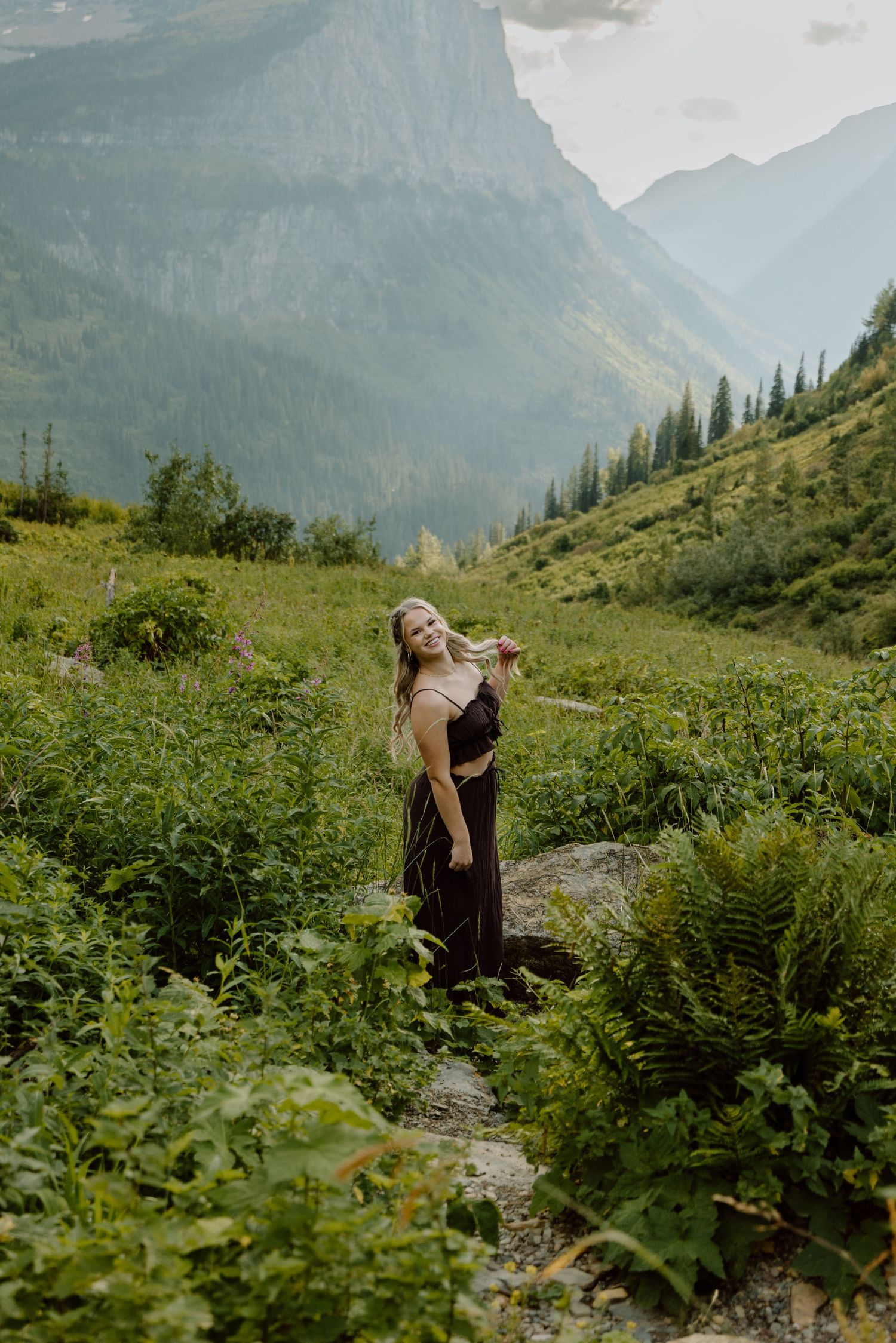 Person enjoying the scenic mountain landscape surrounded by lush greenery and wildflowers on a hiking trail.