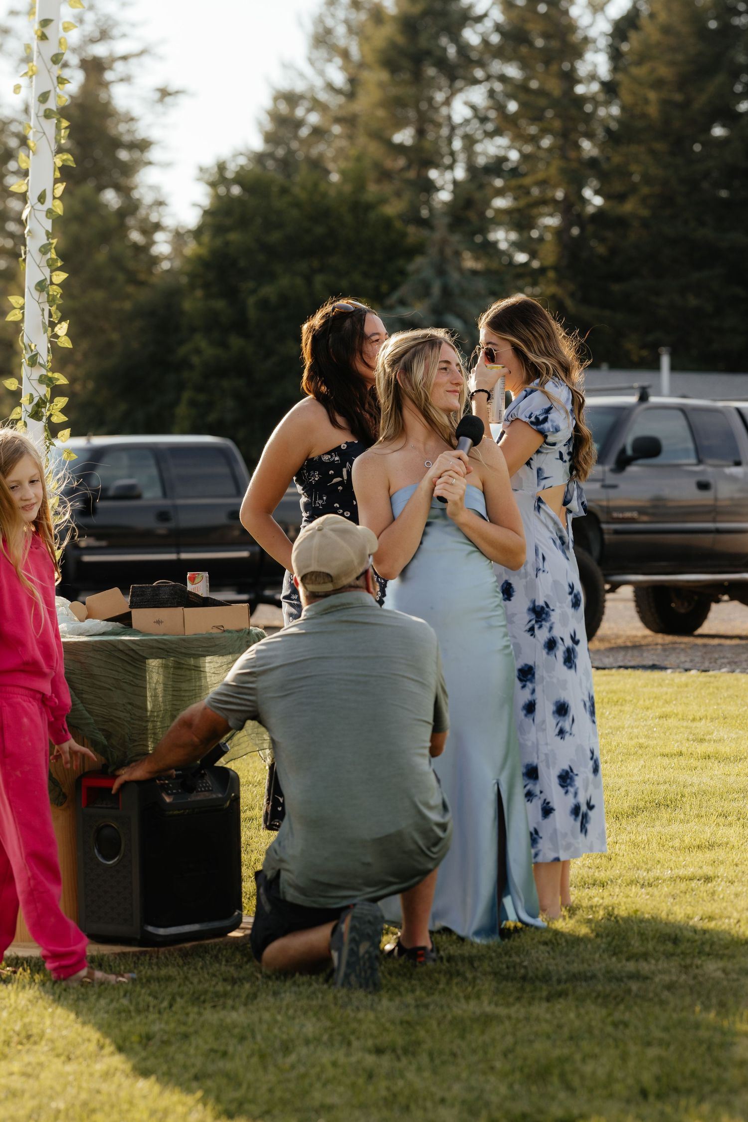 A group of people gather around a vintage car in a grassy field during golden hour.