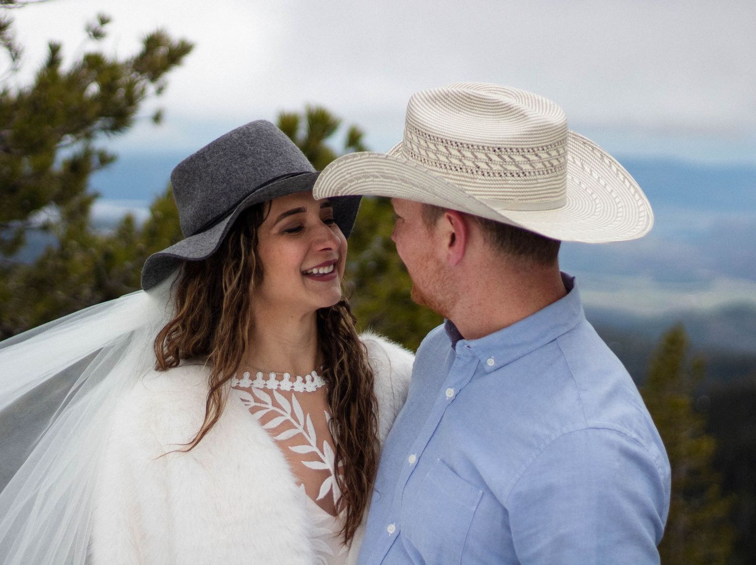 A couple in western attire shares romantic moments during their mountain wedding photoshoot with scenic views.