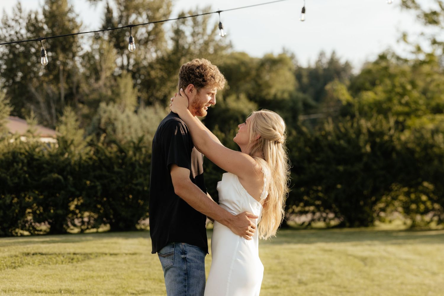 A couple shares a romantic dance in a field decorated with string lights at golden hour.