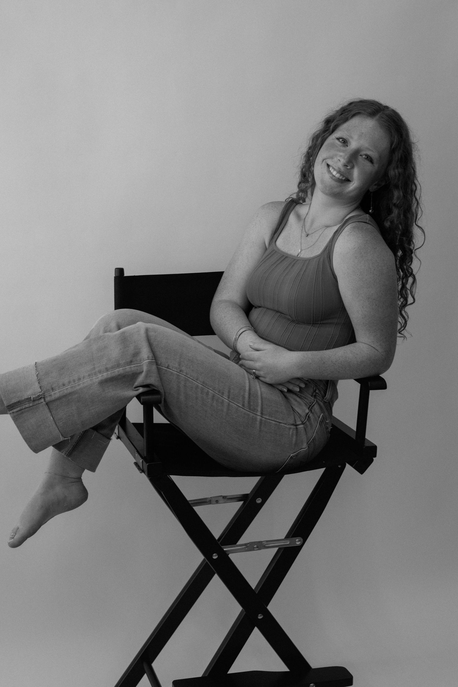 Artistic black and white photo of someone lounging on a director's chair in casual attire.