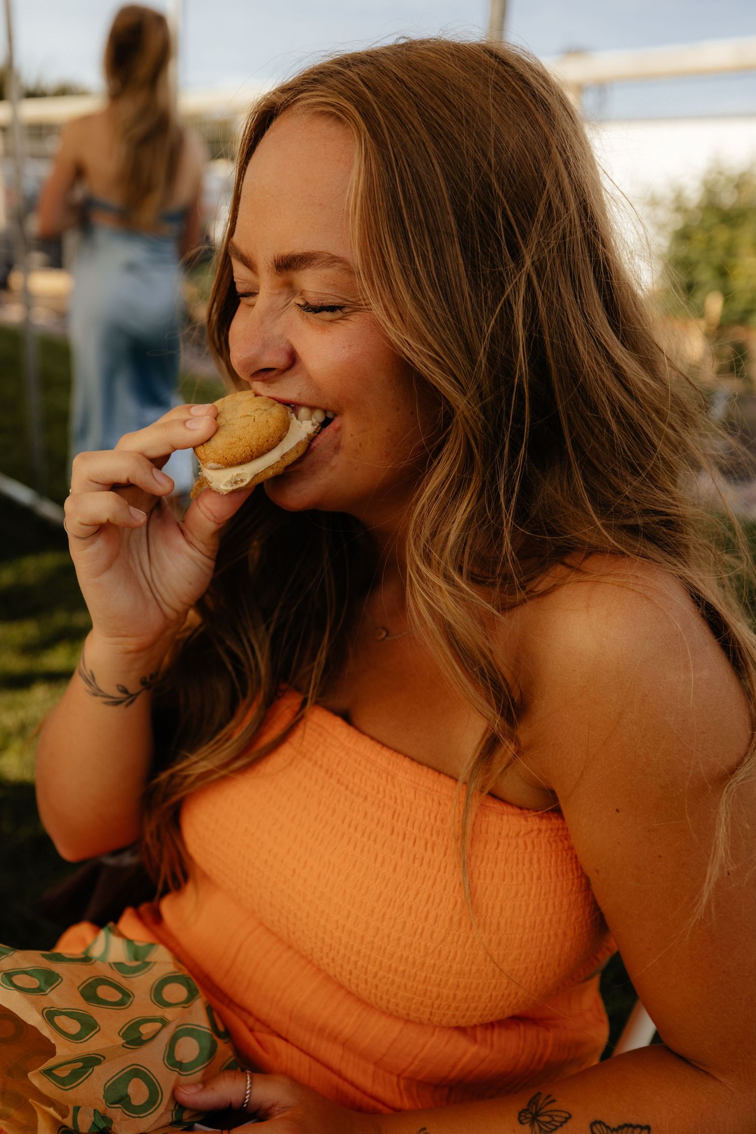 A person in an orange top takes a bite of a cookie in a series of candid sunset photos.