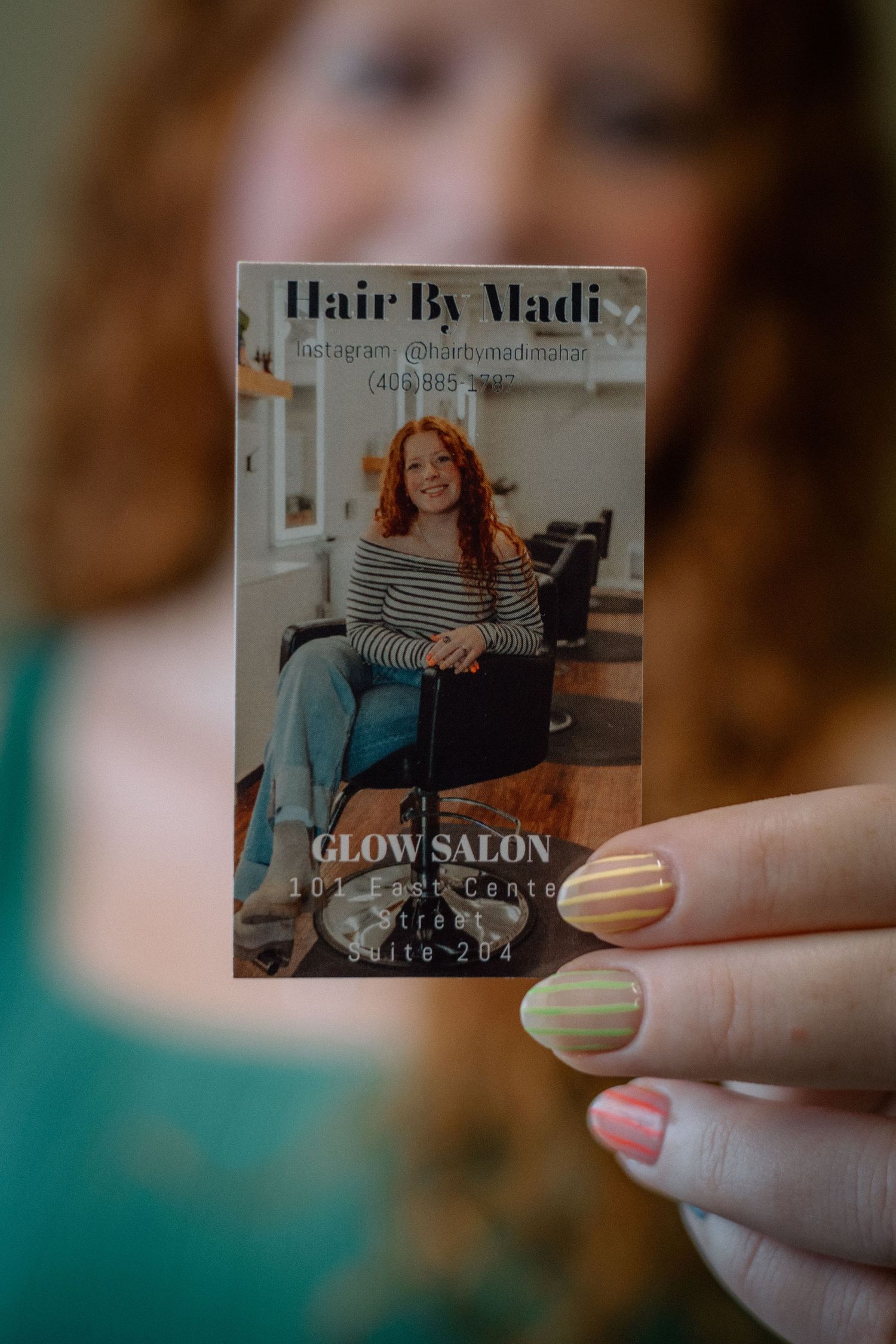 A hand holds up small business cards or promotional materials for a hair salon against a blurred background.