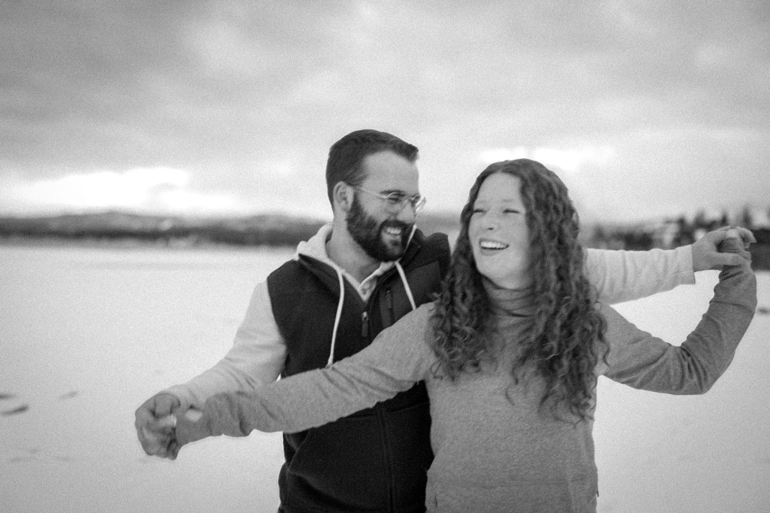 A couple laughs together in black and white against a winter backdrop.