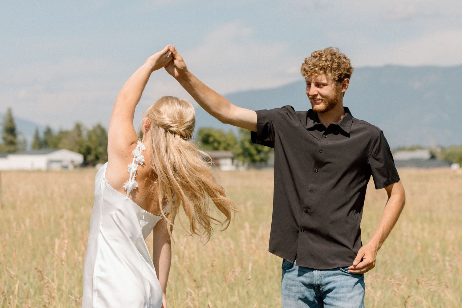 Dancing couple in casual wear spinning together in a summer field.