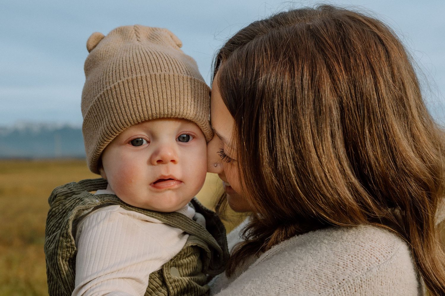 A tender moment between parent and child in warm earth tones against a natural outdoor setting.
