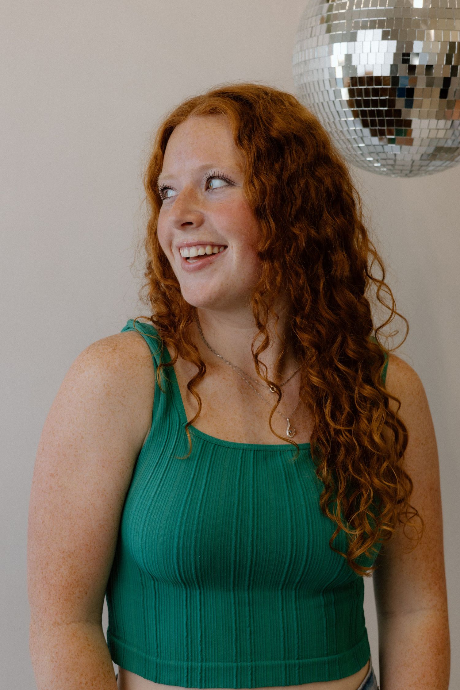 Person in a green sleeveless top poses playfully under a disco ball.