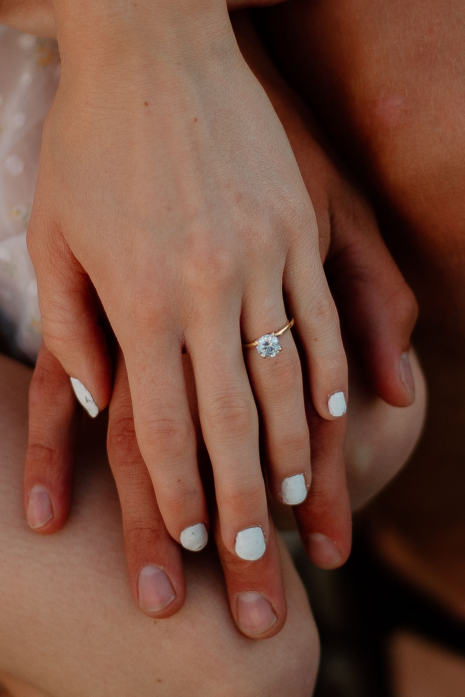 Close-up of hands with white nail polish and engagement ring.