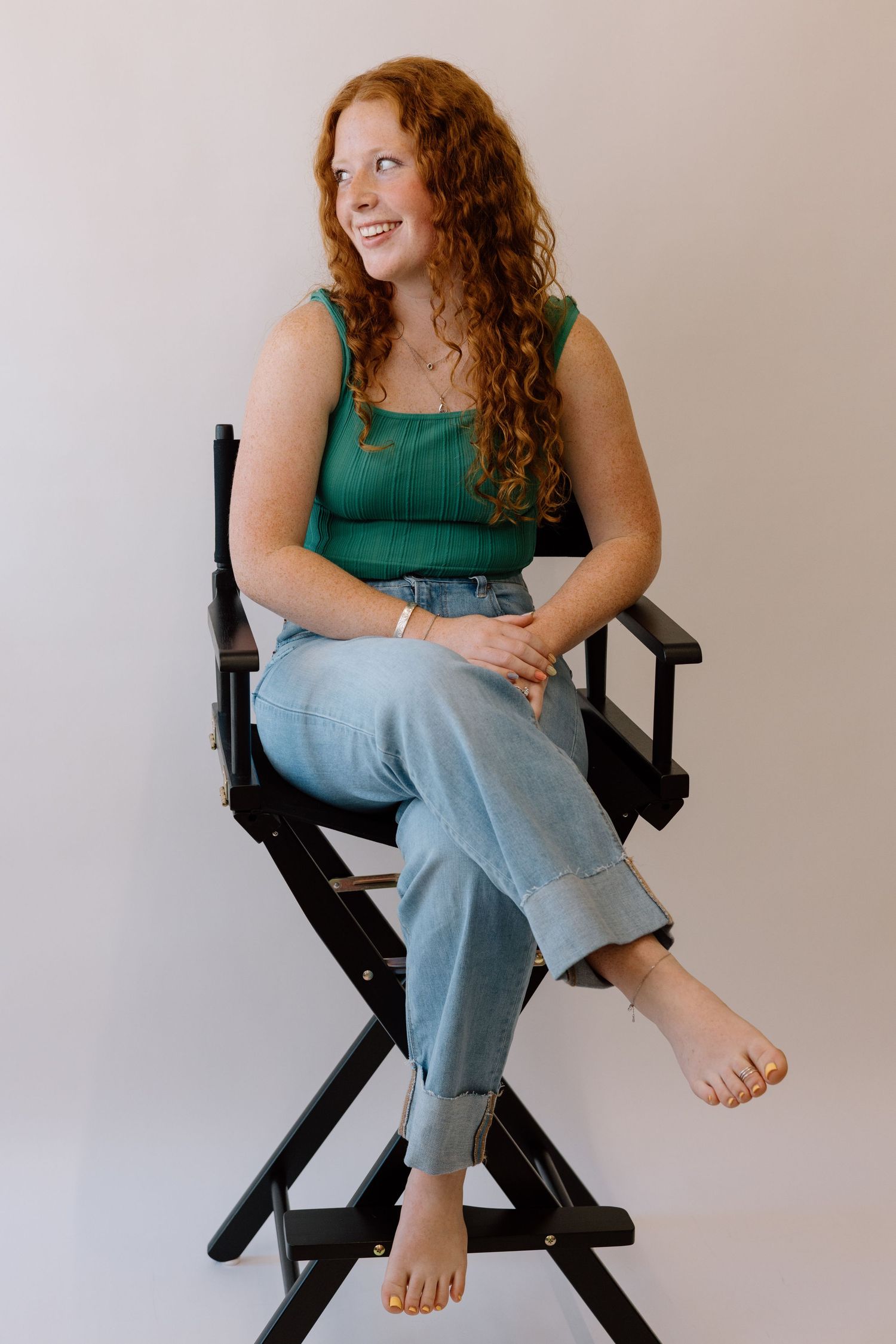 Person with curly red hair in green top sitting casually in director's chair showing various playful poses.