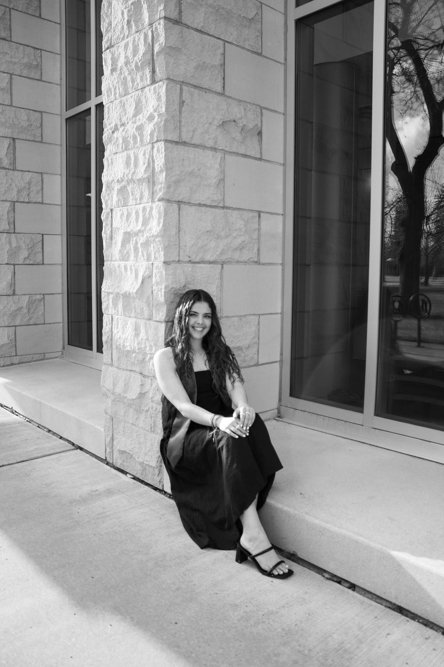 Person in black dress posing against white stone building wall.