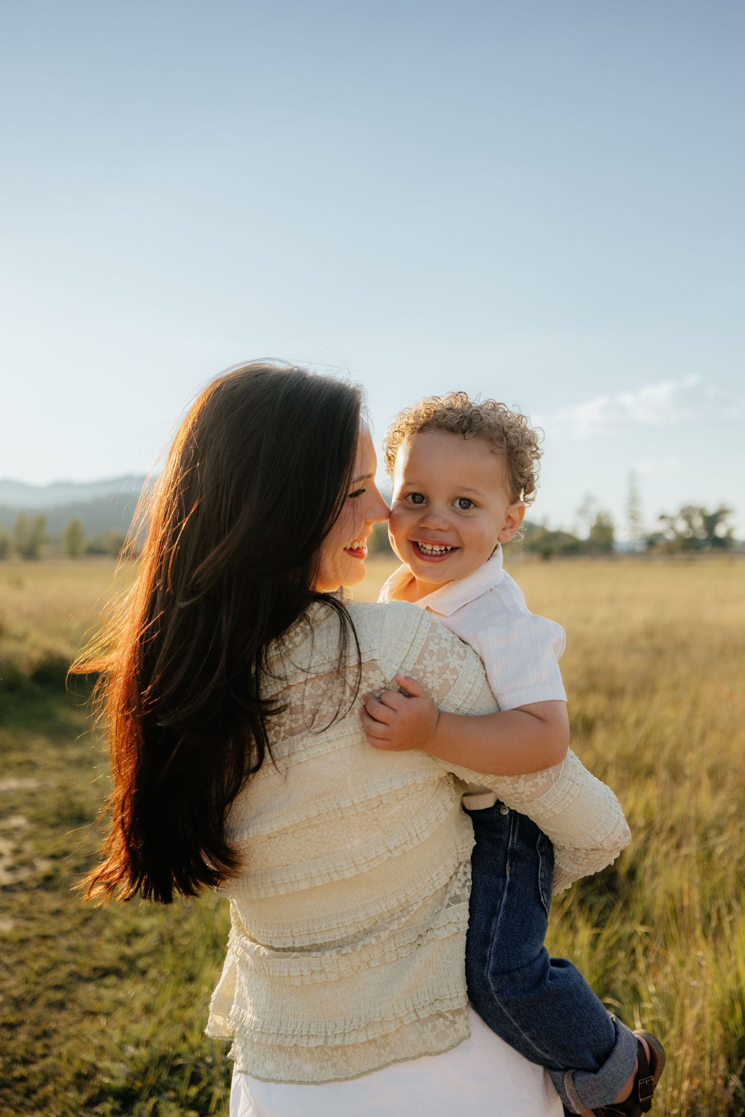 A tender moment between parent and child playing together in a golden sunlit field at sunset.