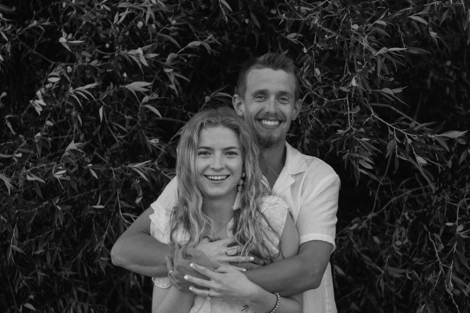 Black and white photo of couple laughing together among foliage.