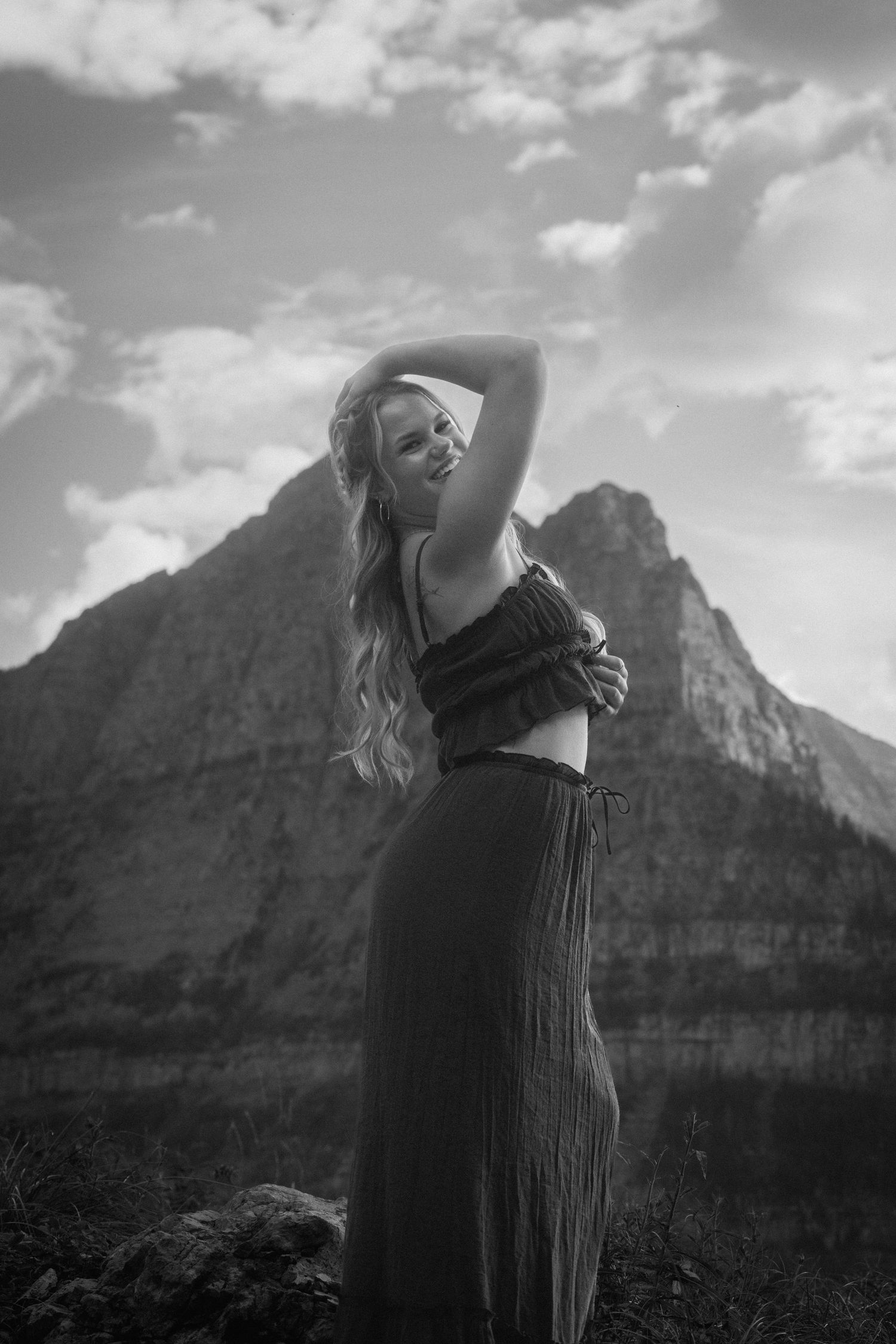 Silhouette against rugged mountain landscape with dramatic cloudy sky in black and white.