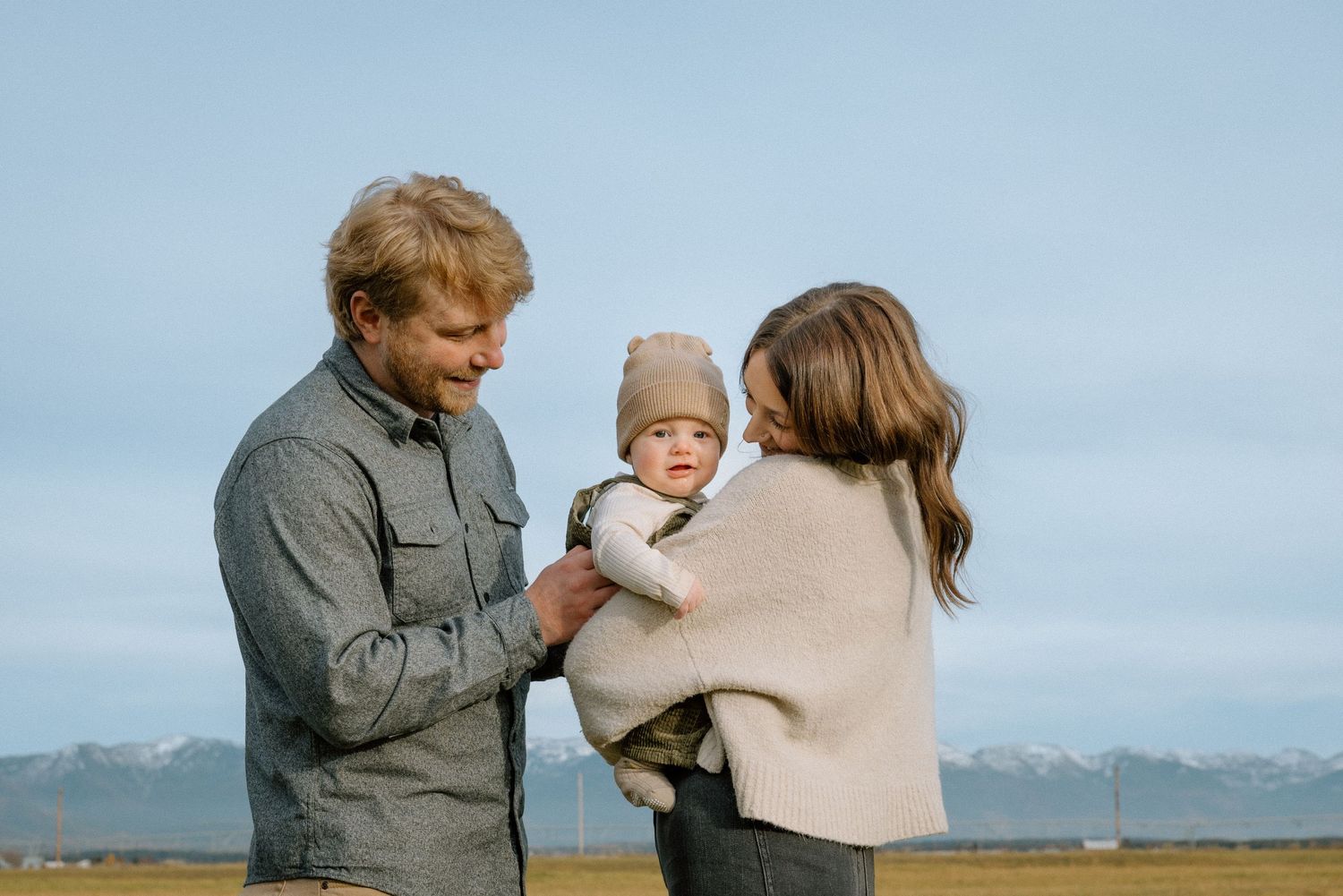 A family shares a tender moment outdoors with snow-capped mountains visible in the distance.
