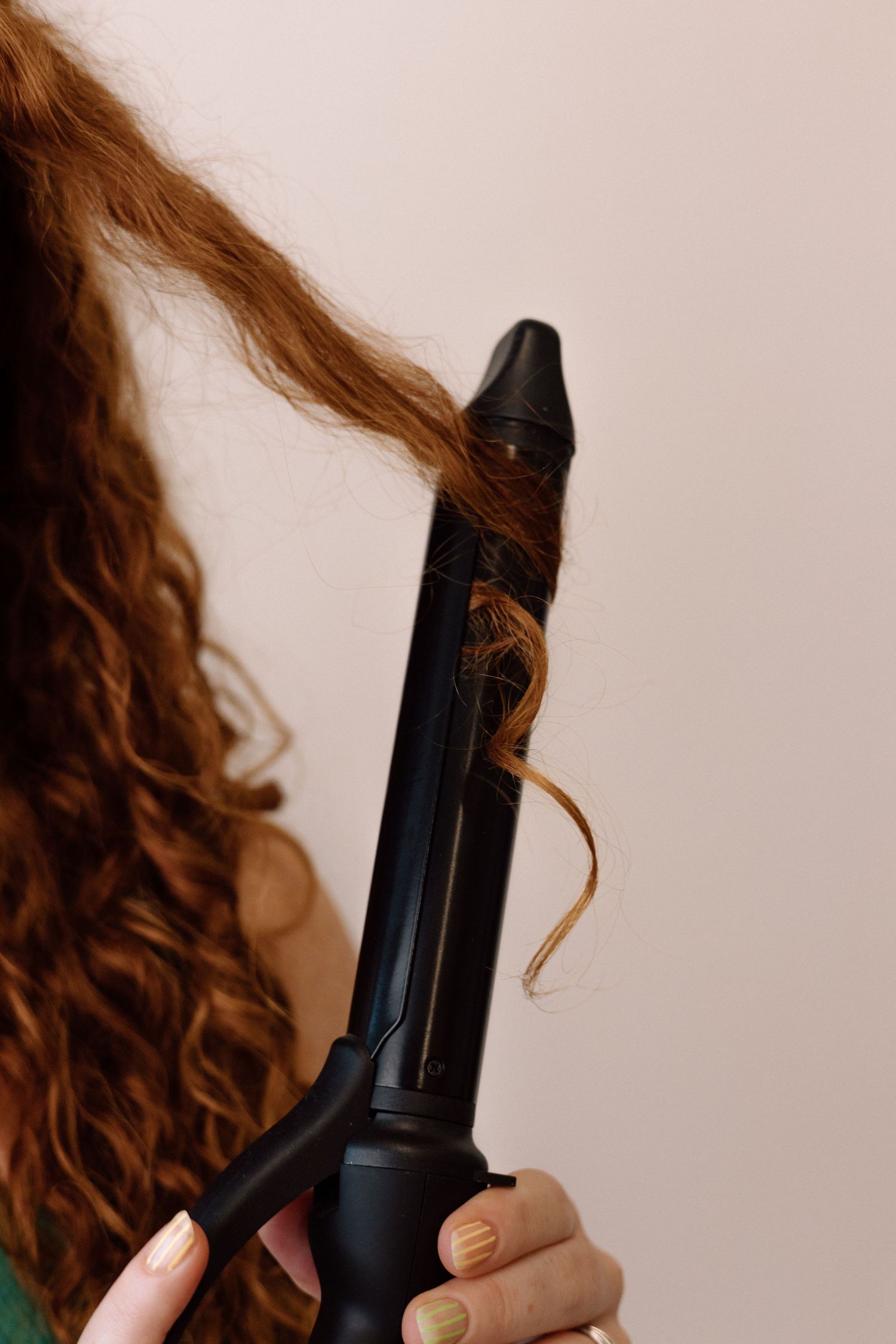 A close-up shot of a black hair styling tool being held against a beige background.