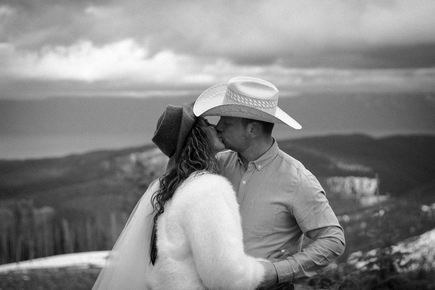A couple shares an intimate moment on a mountaintop overlook in black and white photography.