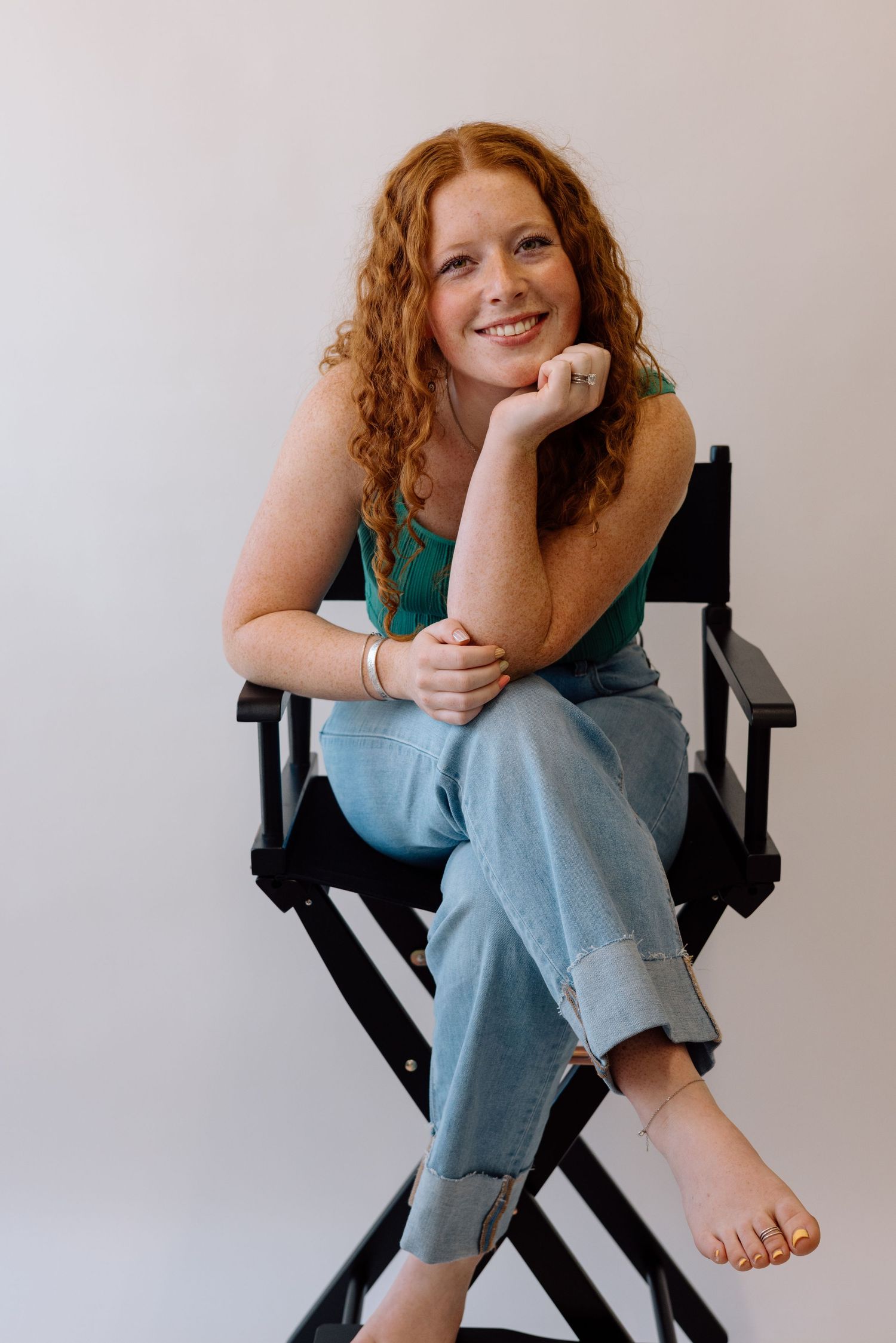 A person in casual attire sitting in a director's chair against a white backdrop.
