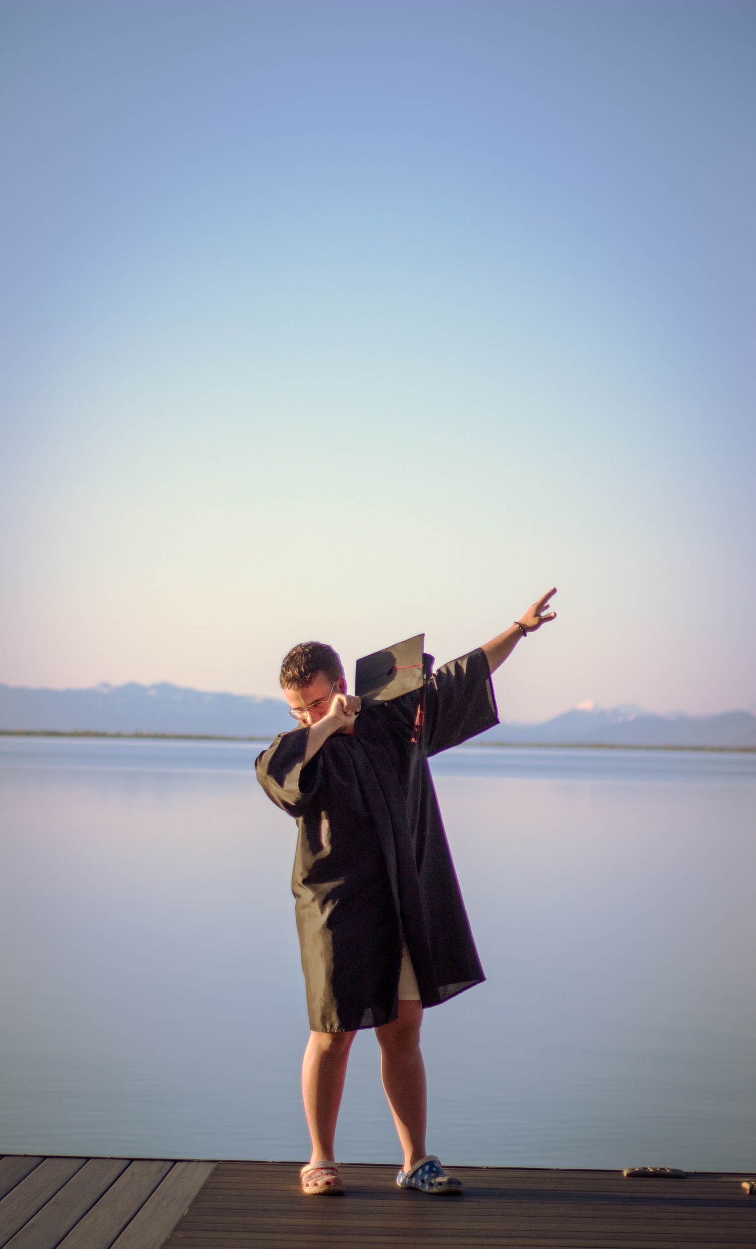 Silhouette of person striking dynamic poses on dock against serene lake view.