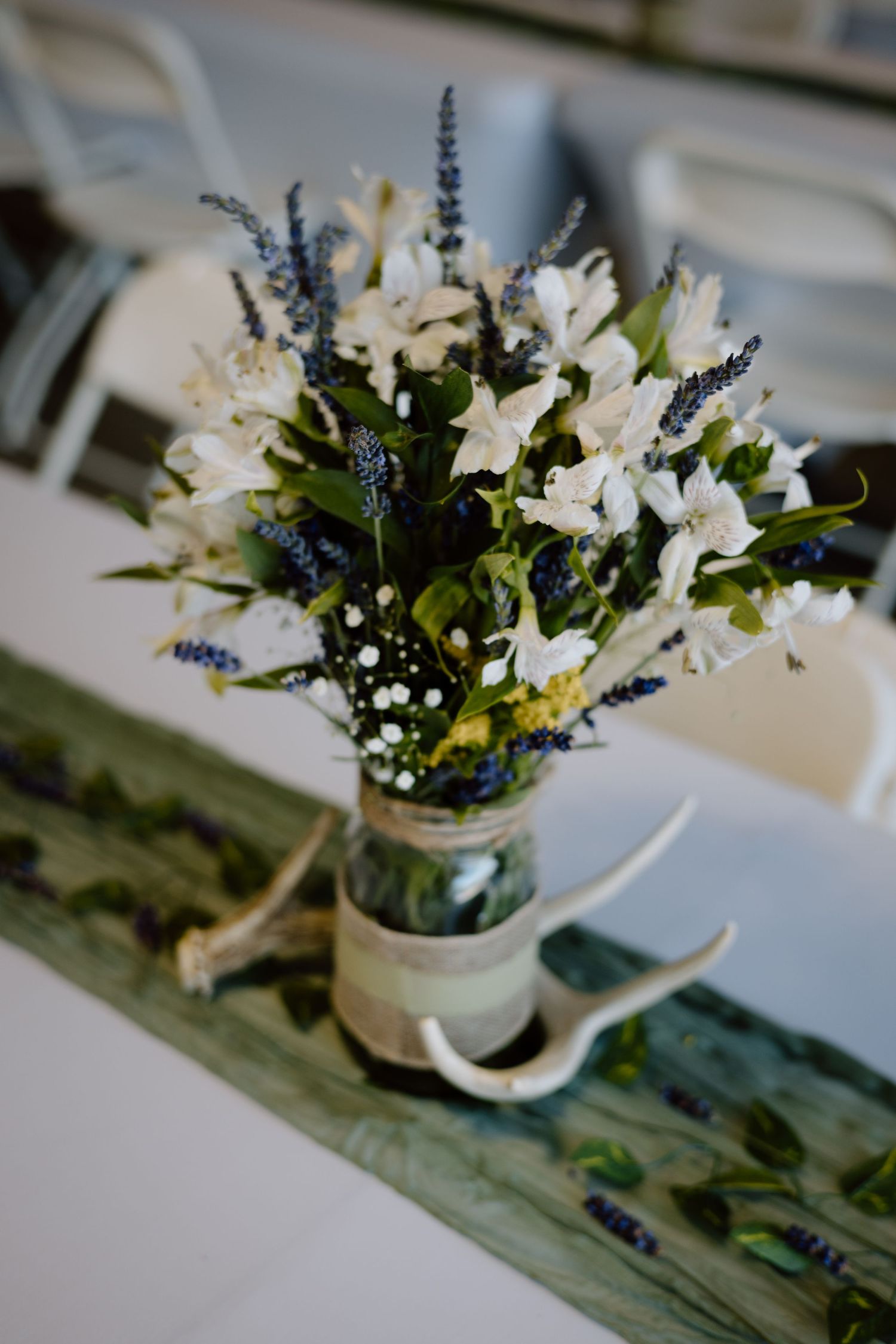 White floral centerpieces with lavender accents arranged in small vases on a rustic wooden surface.