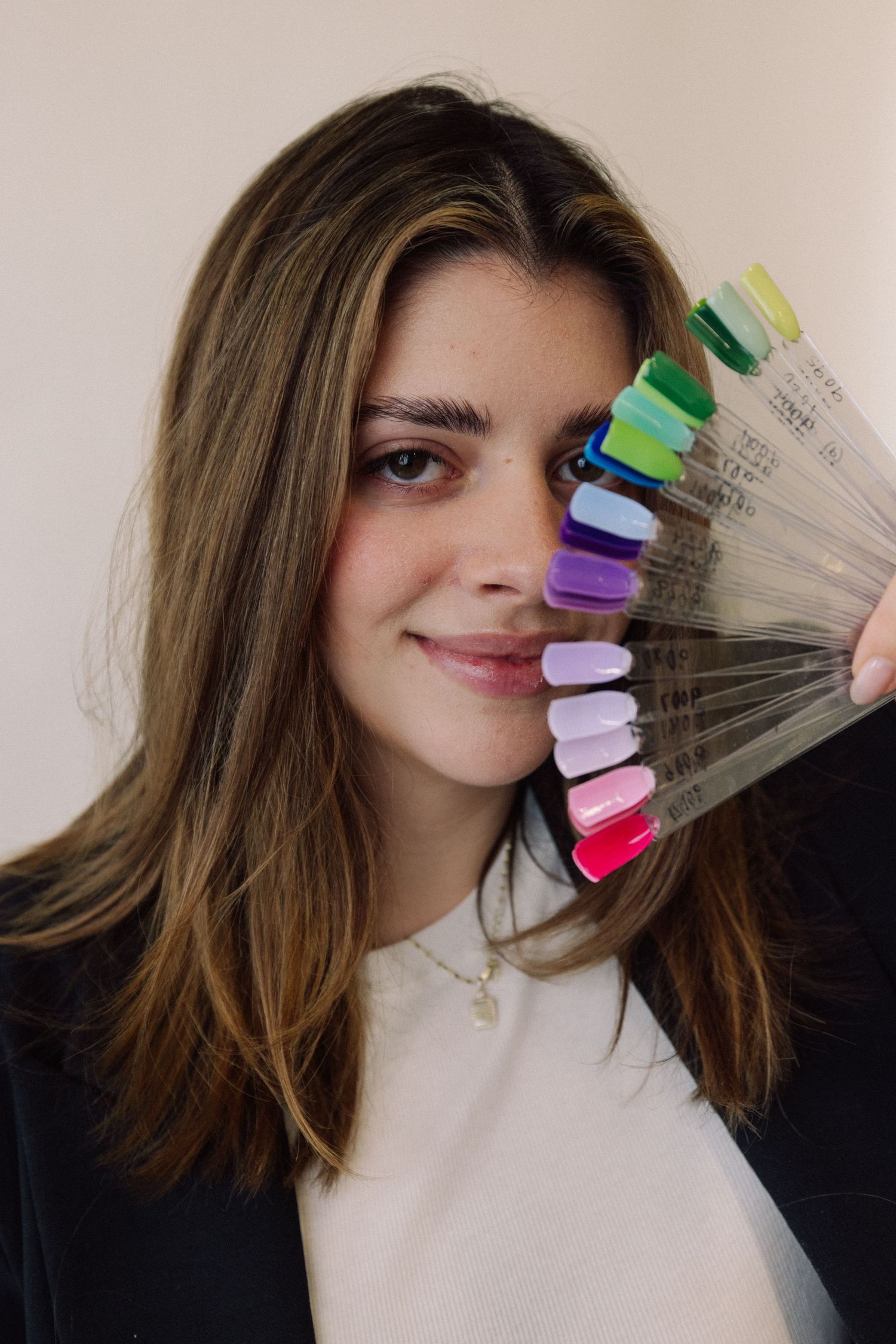 A series of colorful nail polish swatches fanned out against brown hair with a black and white outfit.