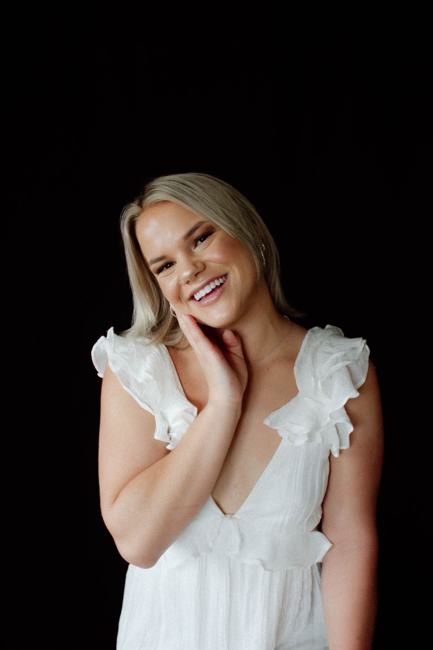 A person in a white ruffled dress laughs joyfully against a dark background.