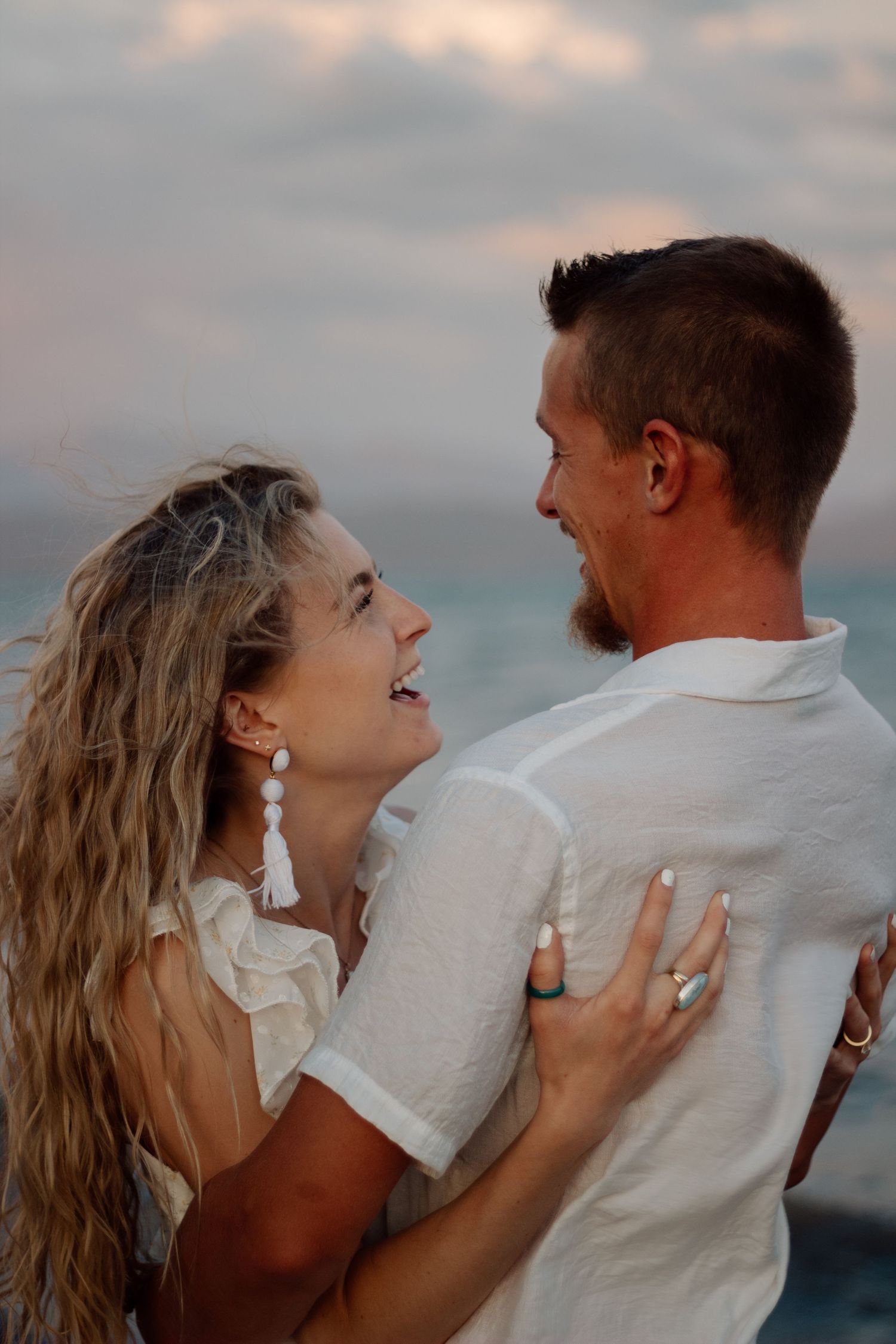 A couple shares an intimate embrace against a cloudy sky during sunset.