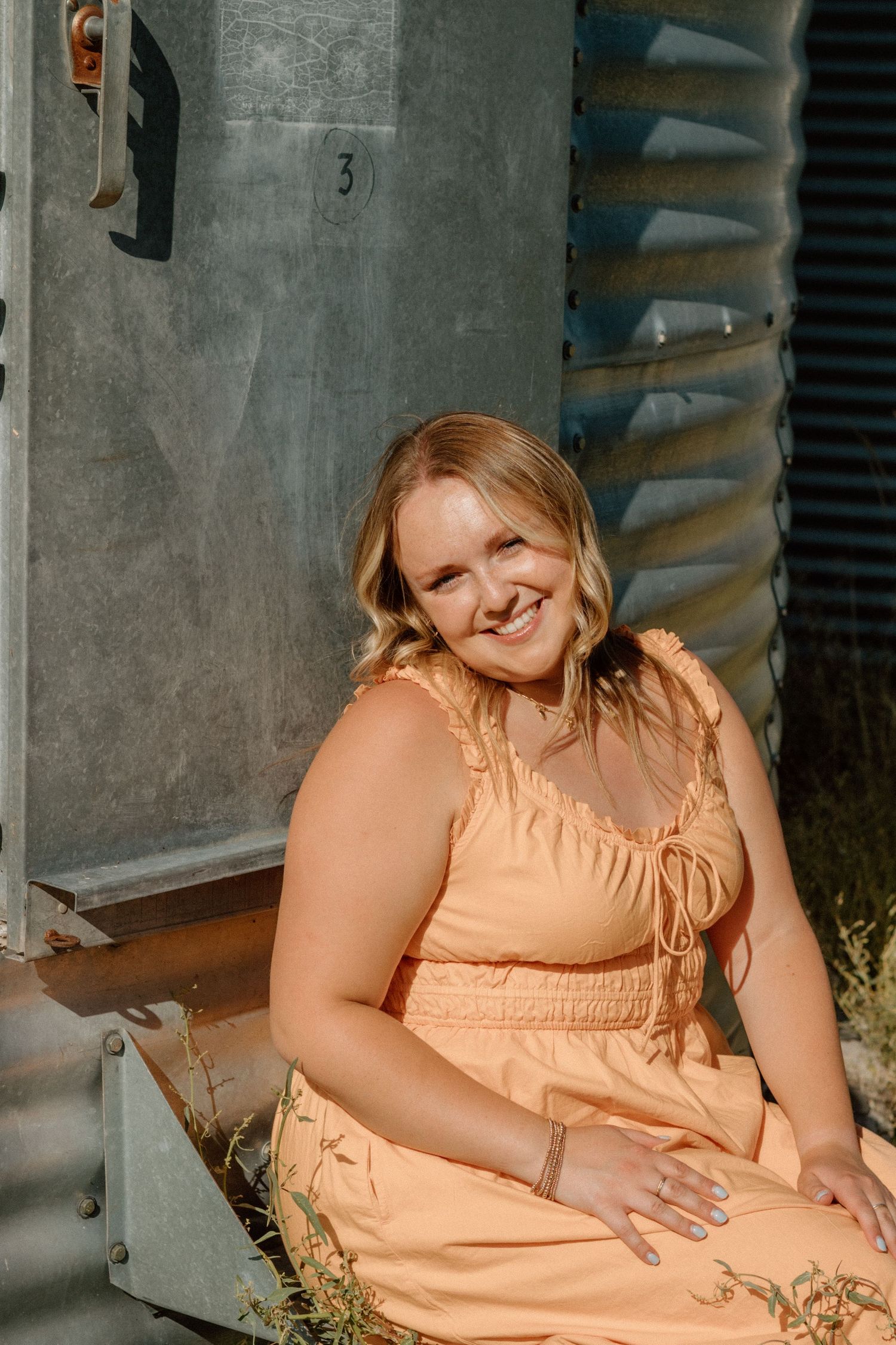 A series of photos showing a person in a peach-colored dress posing against an industrial background.