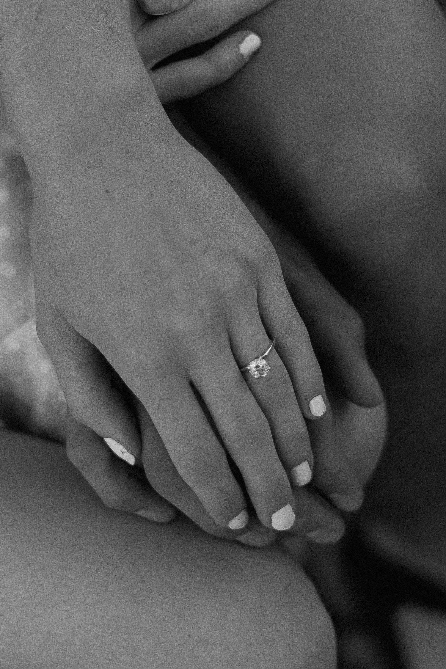 Close-up black and white photograph of hands with white nail polish resting gently on a surface.