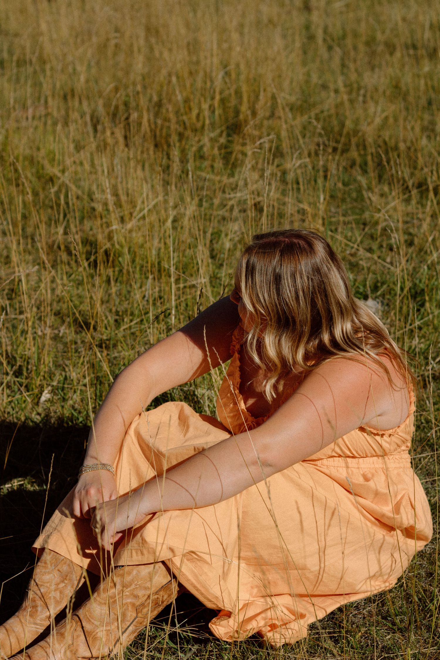 Person in a peach-colored dress lying on grass in a dreamy outdoor setting.