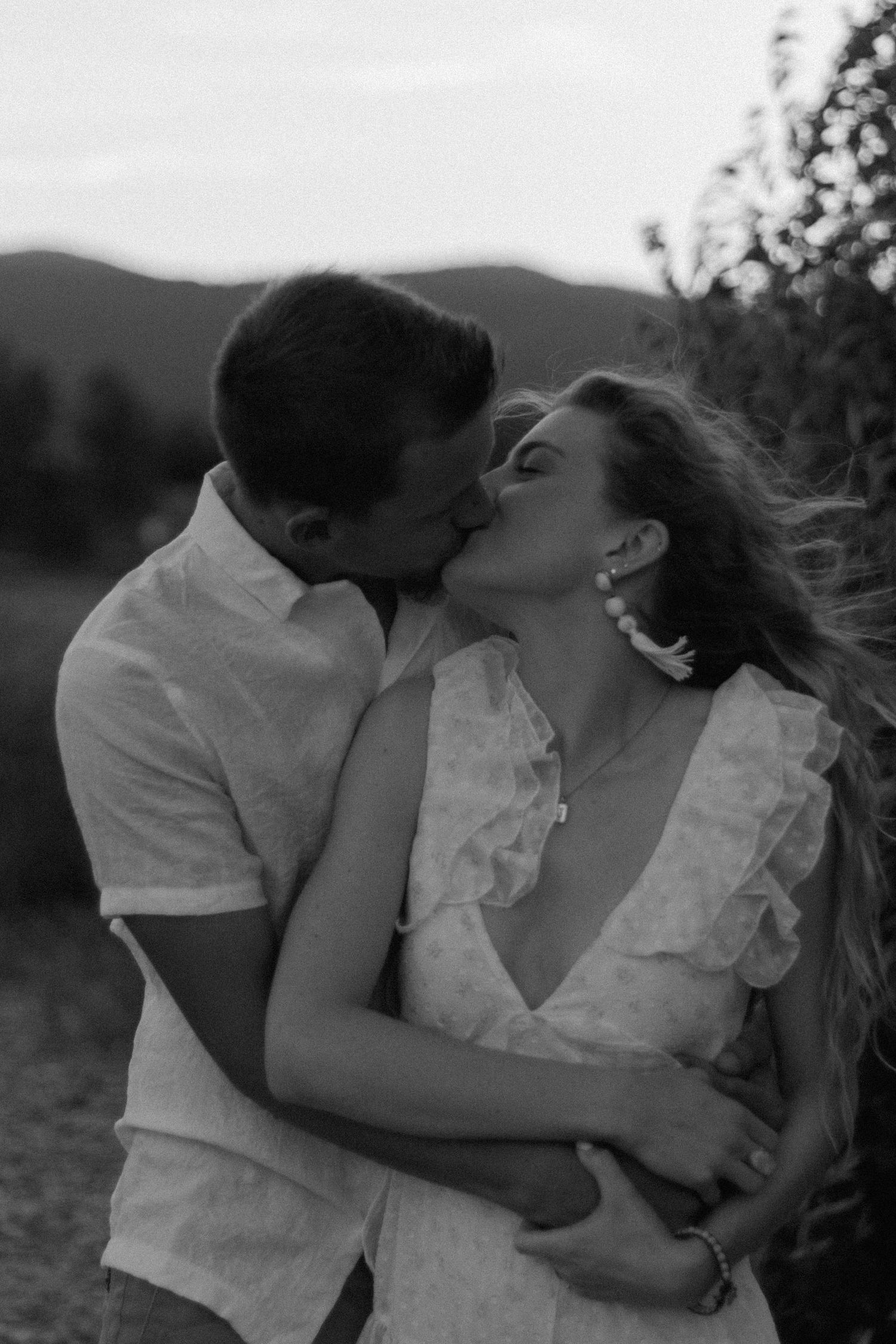 A romantic couple shares intimate moments against a scenic mountain backdrop during sunset.