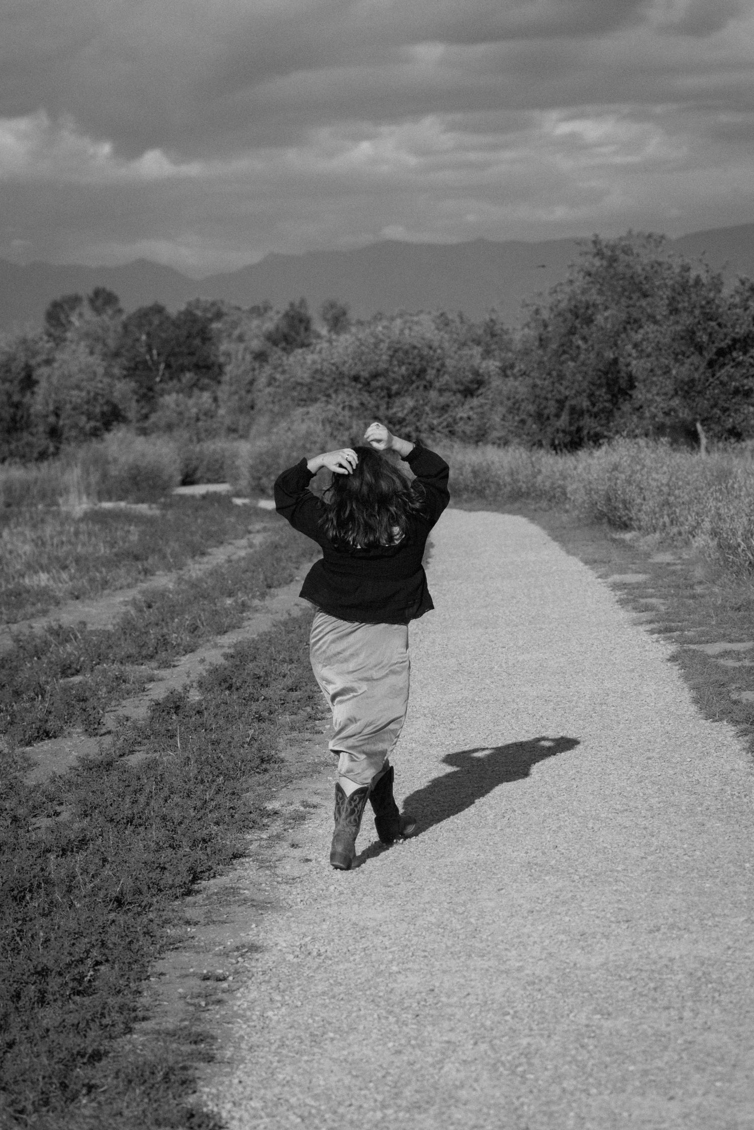 Person dancing and twirling on a gravel path in black and white.