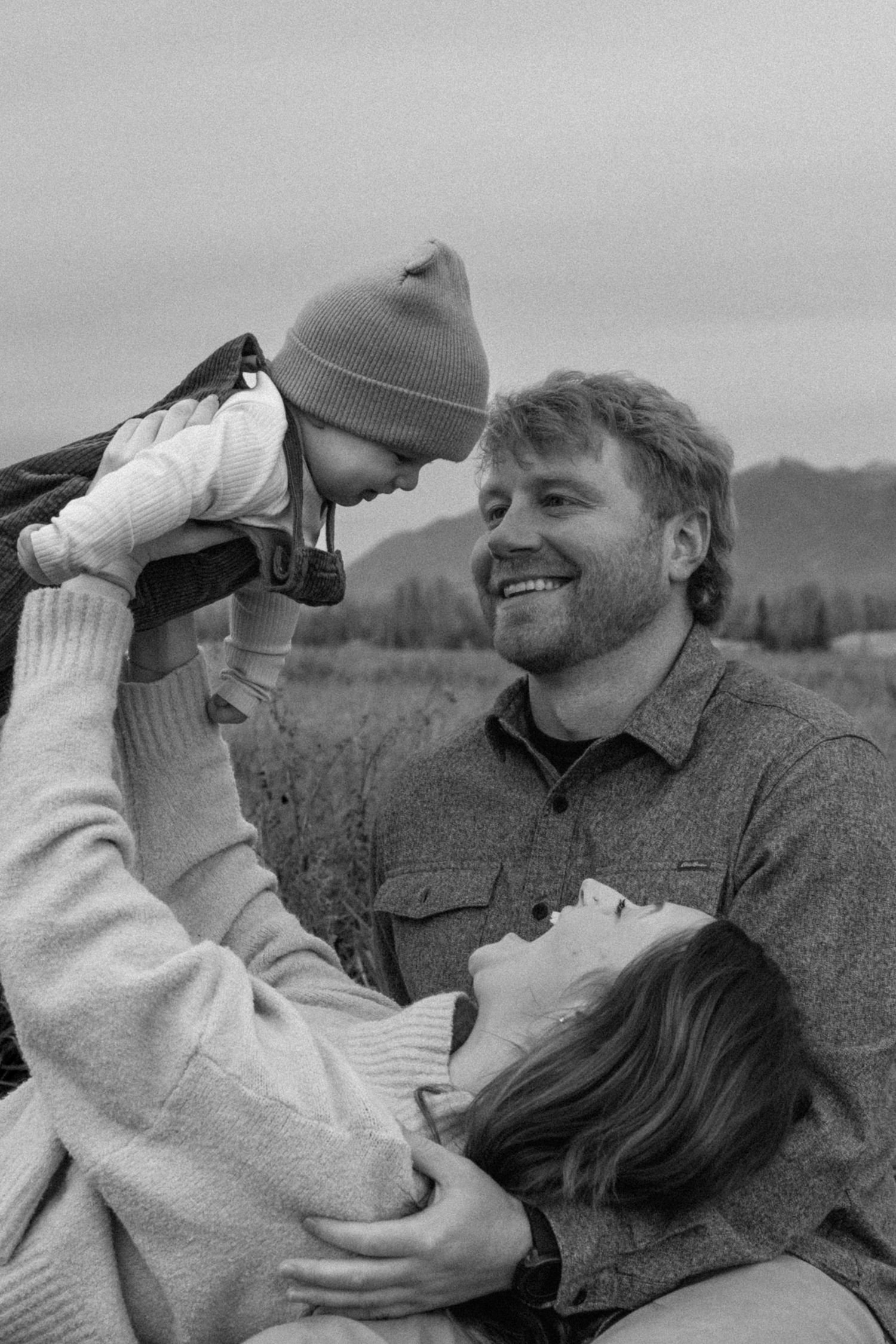 A family shares a joyful moment together in black and white as they play outdoors with mountains in the background.