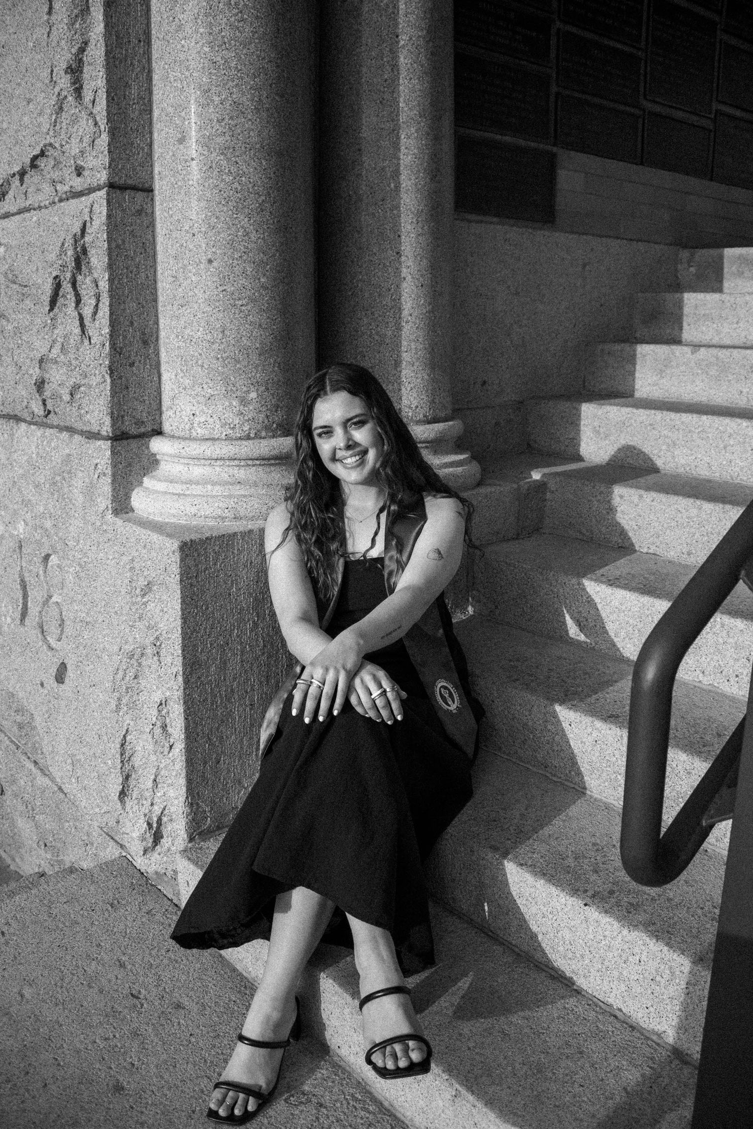 Black and white portrait of graduate sitting in stone archway.