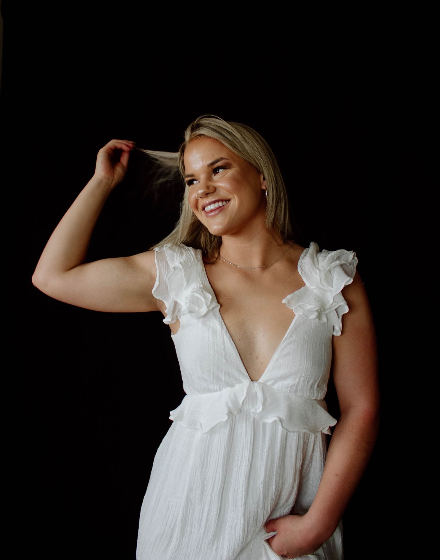 Portrait in white ruffled dress against dark background.