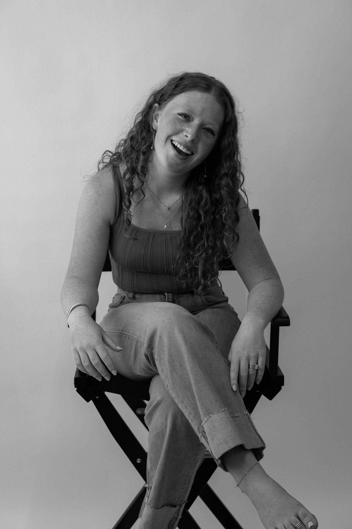 A person sitting in a chair laughs and smiles during a candid black and white photoshoot.